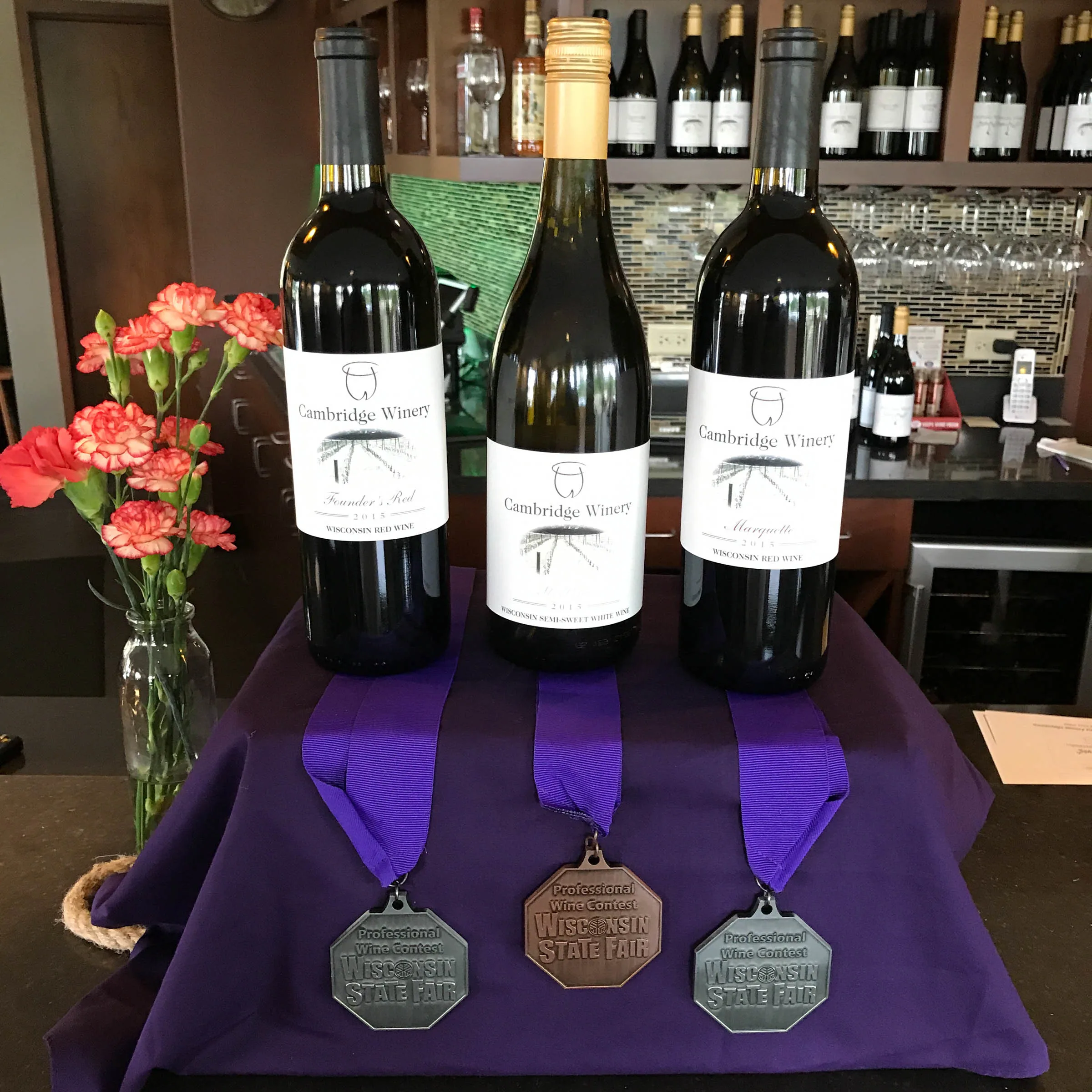 A display of local prize-winning boutique red and white wines from Cambridge Winery in Madison, featuring their award medals from the Wisconsin State Fair.