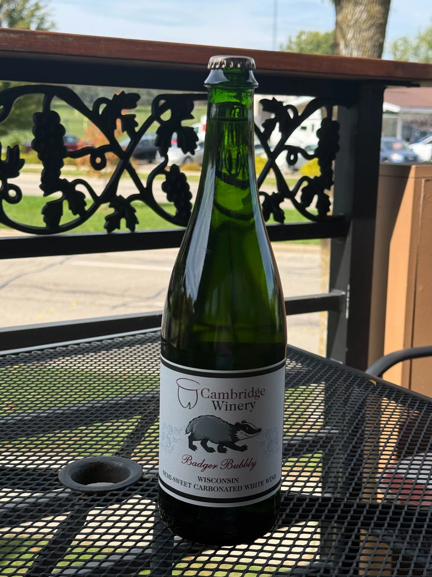 A bottle of Badger Bubbly semi-sweet carbonated white wine by Cambridge Winery sitting on an outdoor patio mesh table.