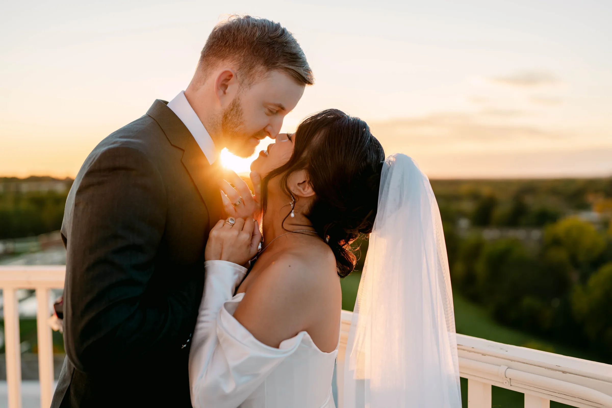 Rooftop golden hour wedding photography in Madison, WI, by Blu Photography & Design LLC, capturing a romantic bride and groom sunset embrace with a dramatic lens flare glowing between them.