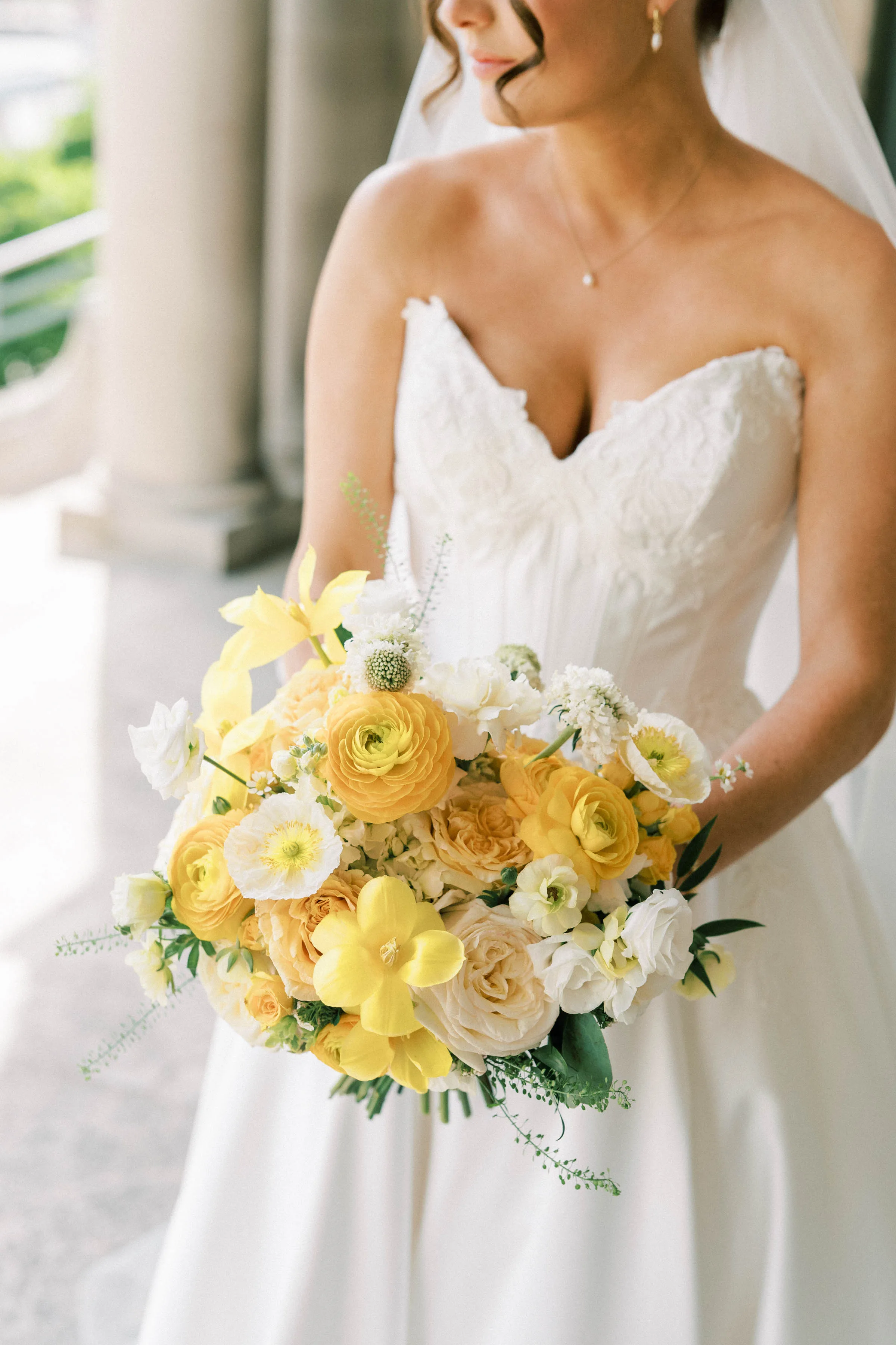Bright yellow and cream wedding bridal bouquet by Cosmic Gardens in Cross Plains, WI, featuring yellow ranunculus, tulips, and white garden roses held by a bride in a strapless gown.