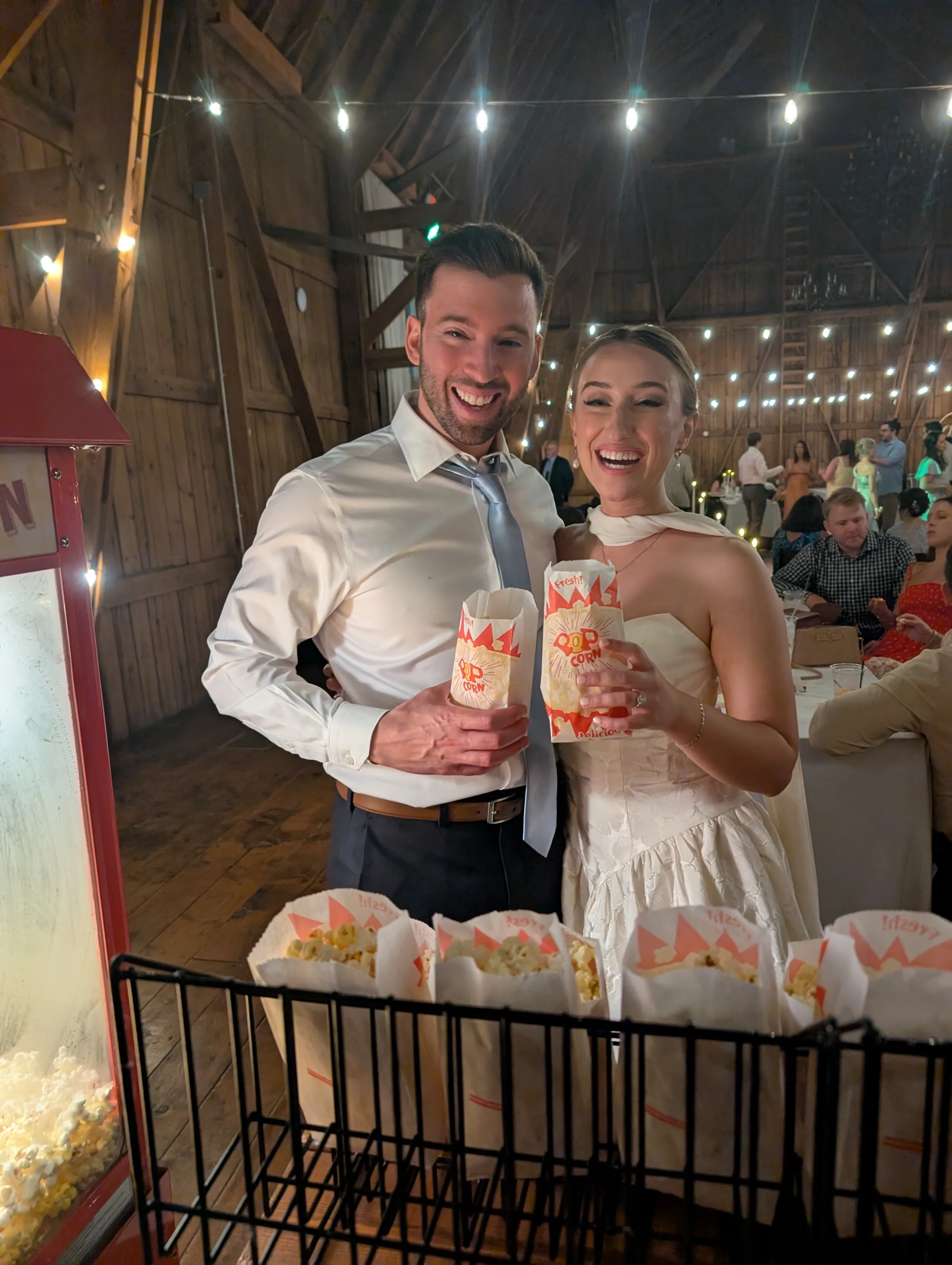 A wedding couple joyfully holds popcorn from Lily's Magical Treats as they enjoy a reception.