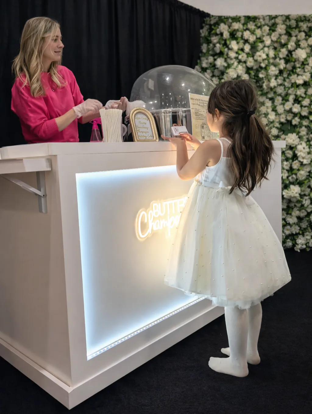 A little girl dressed for a wedding adoringly looks at the cotton candy displayed on a cotton candy cart from Lily's Magical Treats.