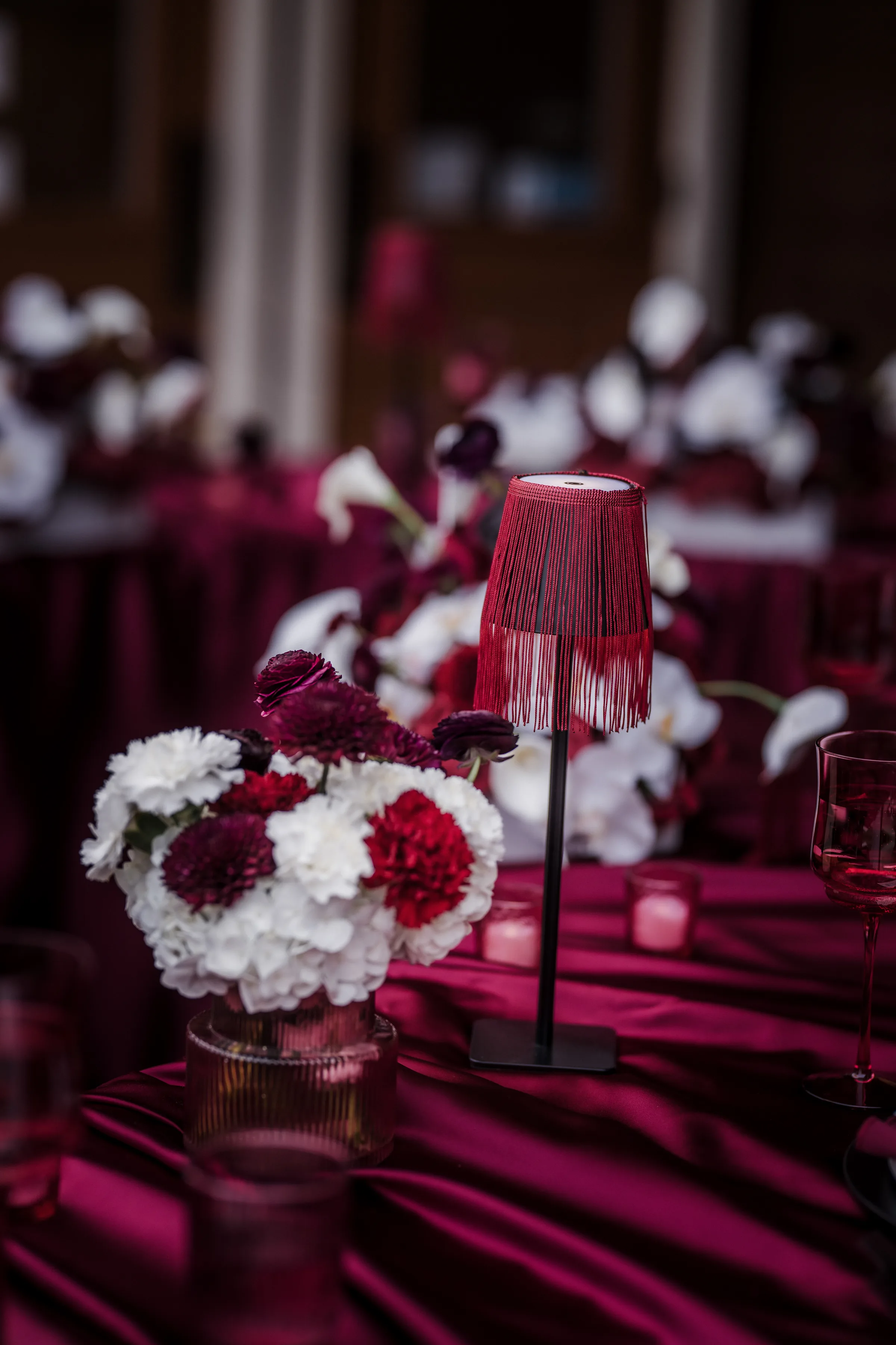 a close-up on a wedding reception table lamp with a burgundy, tasseled lampshade