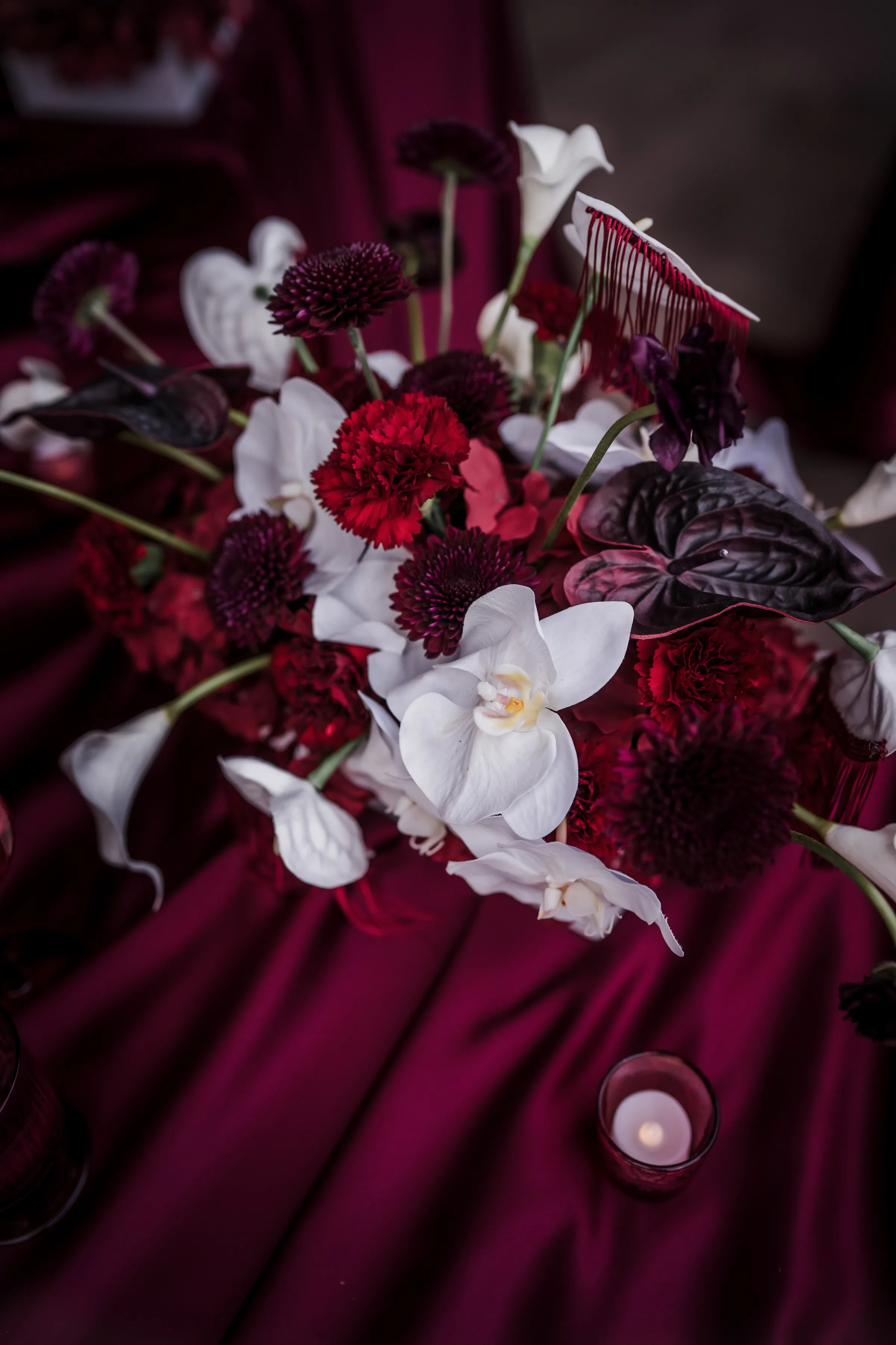 moody floral centerpieces by Melody Rose Designs with white phalaenopsis orchids, white and deep burgundy anthurium, burgundy ranunculus, red dianthus, cascading burgundy amaranthus, and moody smokebush foliage