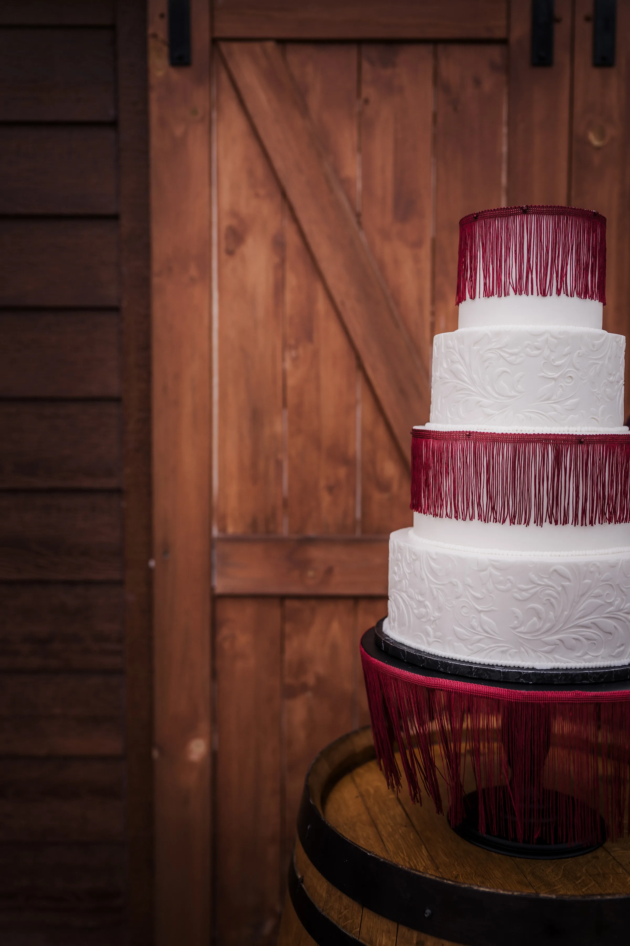 a white, four tier, textured wedding cake from Craig's Cake Shop with burgundy tassels around the second and top layers