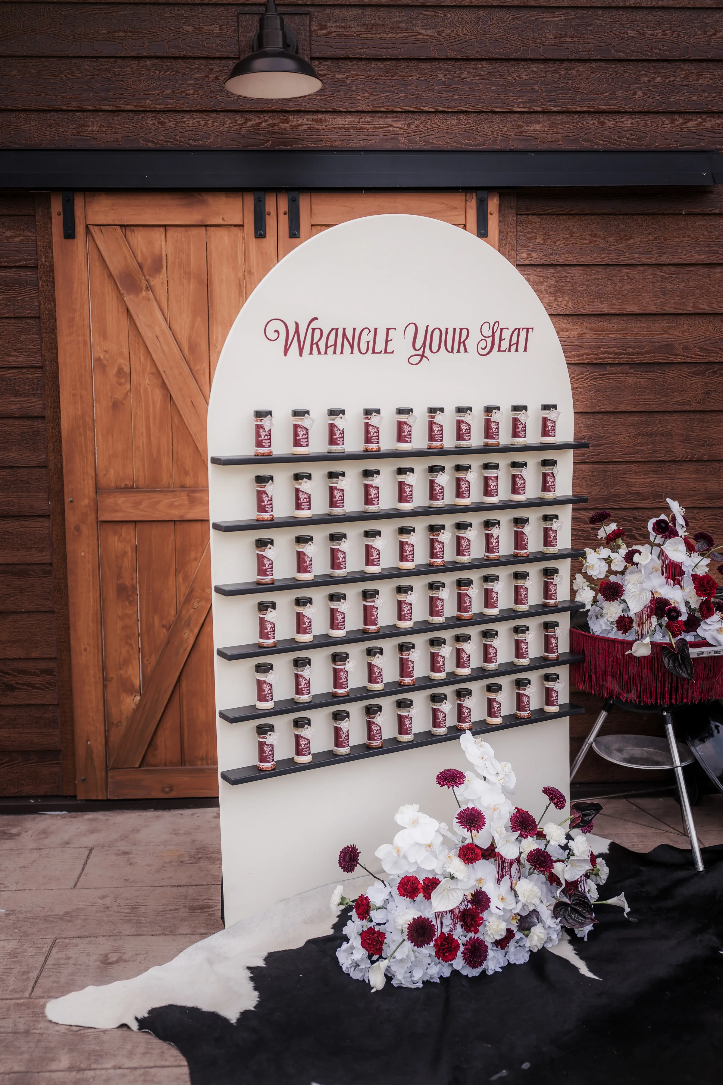 an interactive seating chart wall with spice jar favors individually tagged by LK Bridal Studio. The seating chart wall says "Wrangle Your Seat"