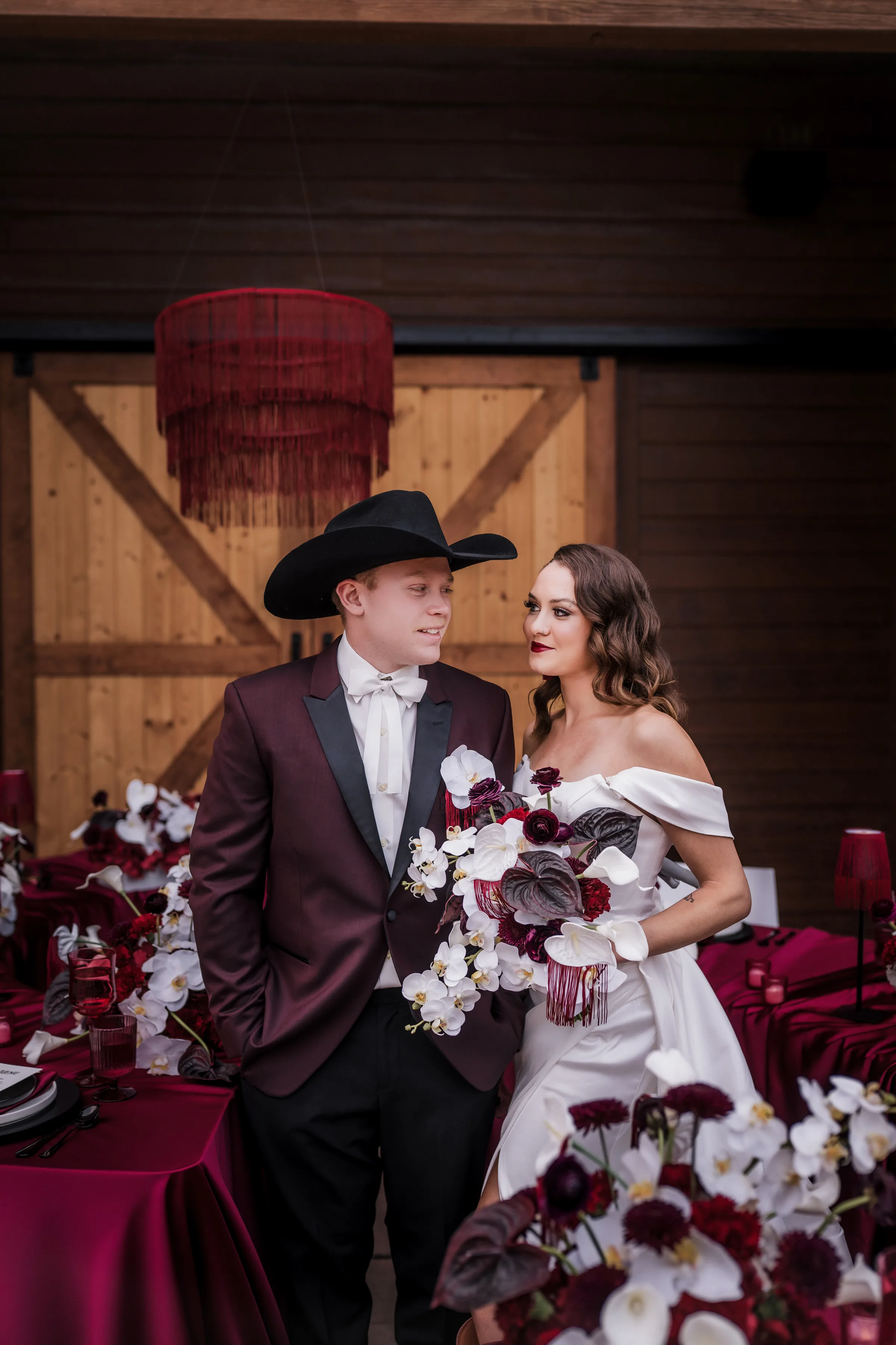 a bride and groom smile at each other at an outdoor reception space at Barnwood Events in Madison, Wisconsin. The couple is fashioned by Charlotte's Bridal & Formal Wear and the bride is holding a moody bouquet from Melody Rose Designs