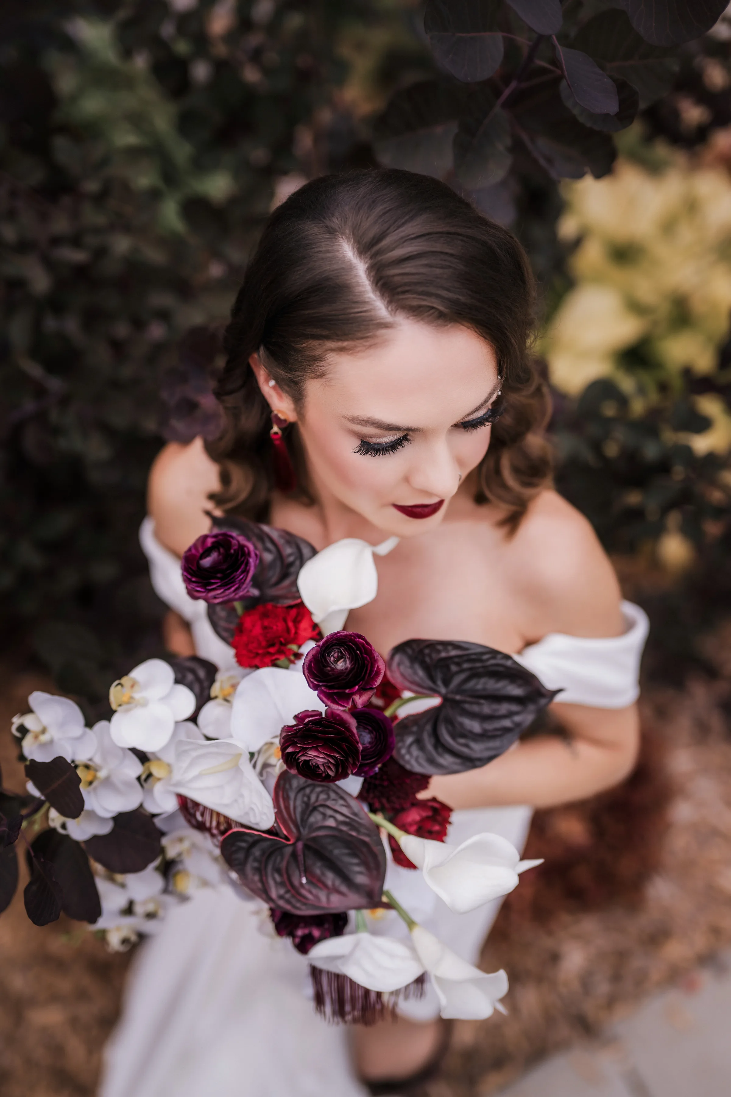 an overhead view of a bride holding a dramatic bouquet from Melody Rose Designs featuring white Phalaenopsis orchids and calla lilies with deep burgundy ranunculus, red carnations, sculptural anthurium, and dark foliage.