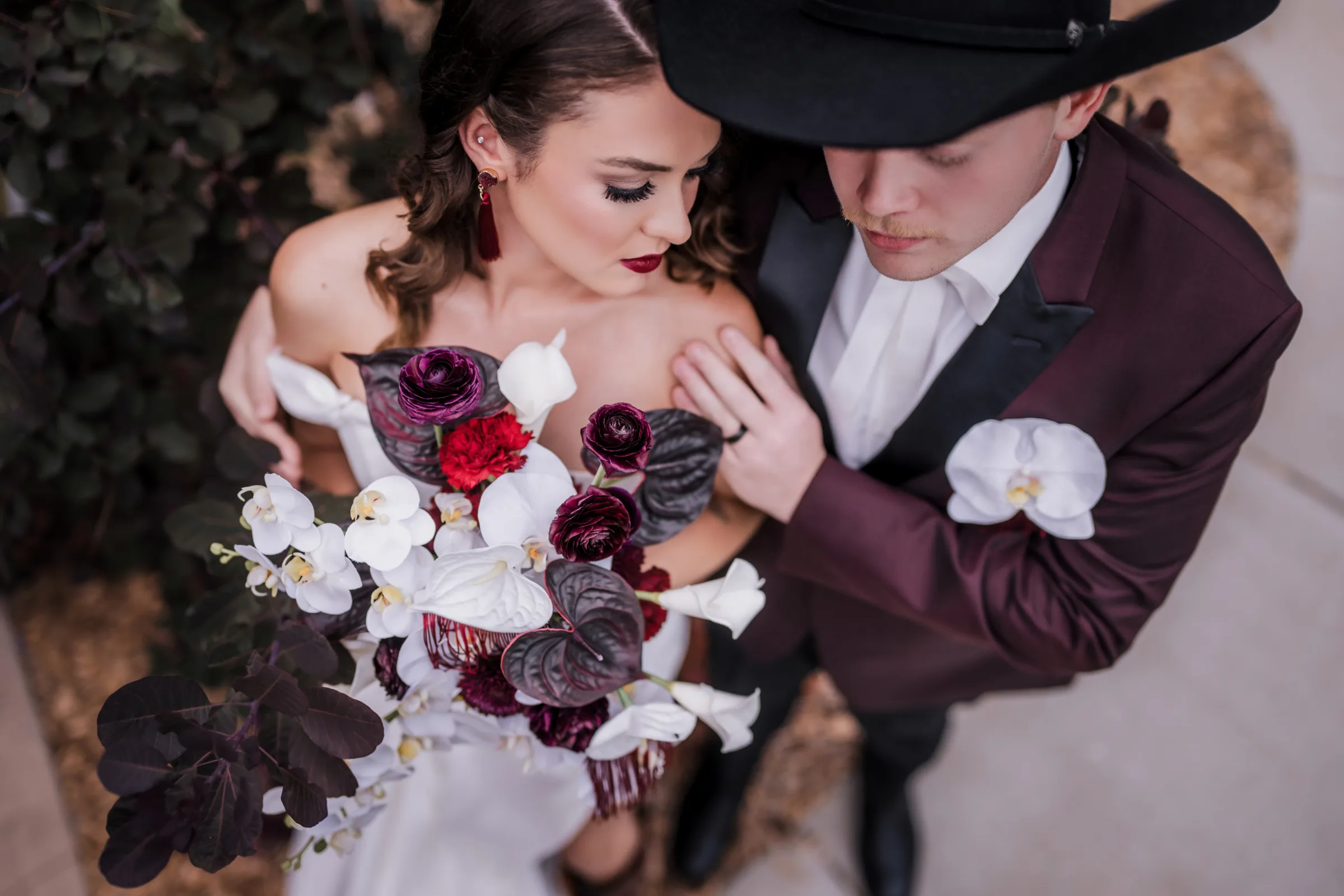 a bride and groom embrace, photographed from above to focus on the bride's moody makeup and bridal bouquet