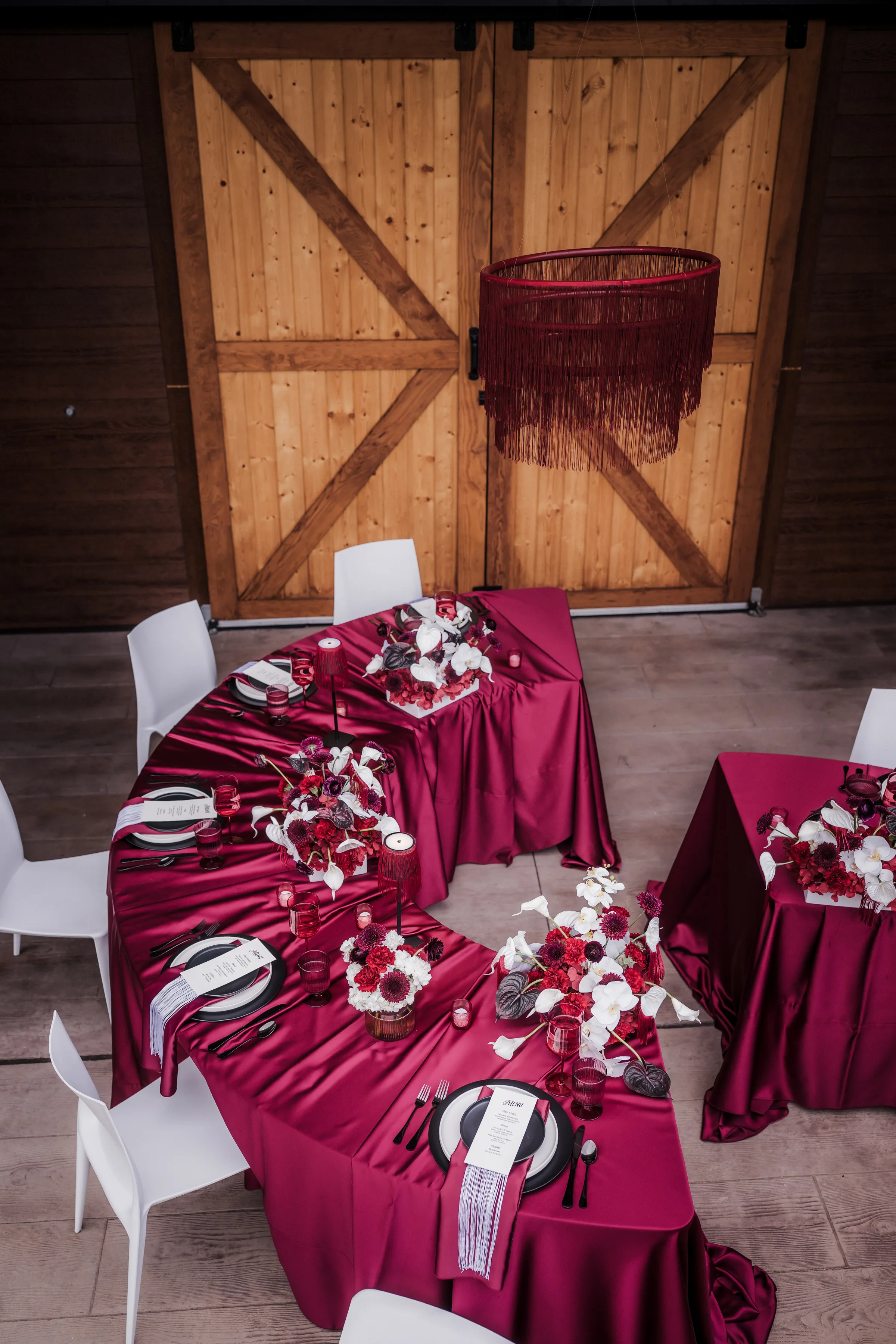 an overhead view of a half-circle reception table draped in a burgundy velvet tablecloth and surrounded with white chairs and layered place settings on one side
