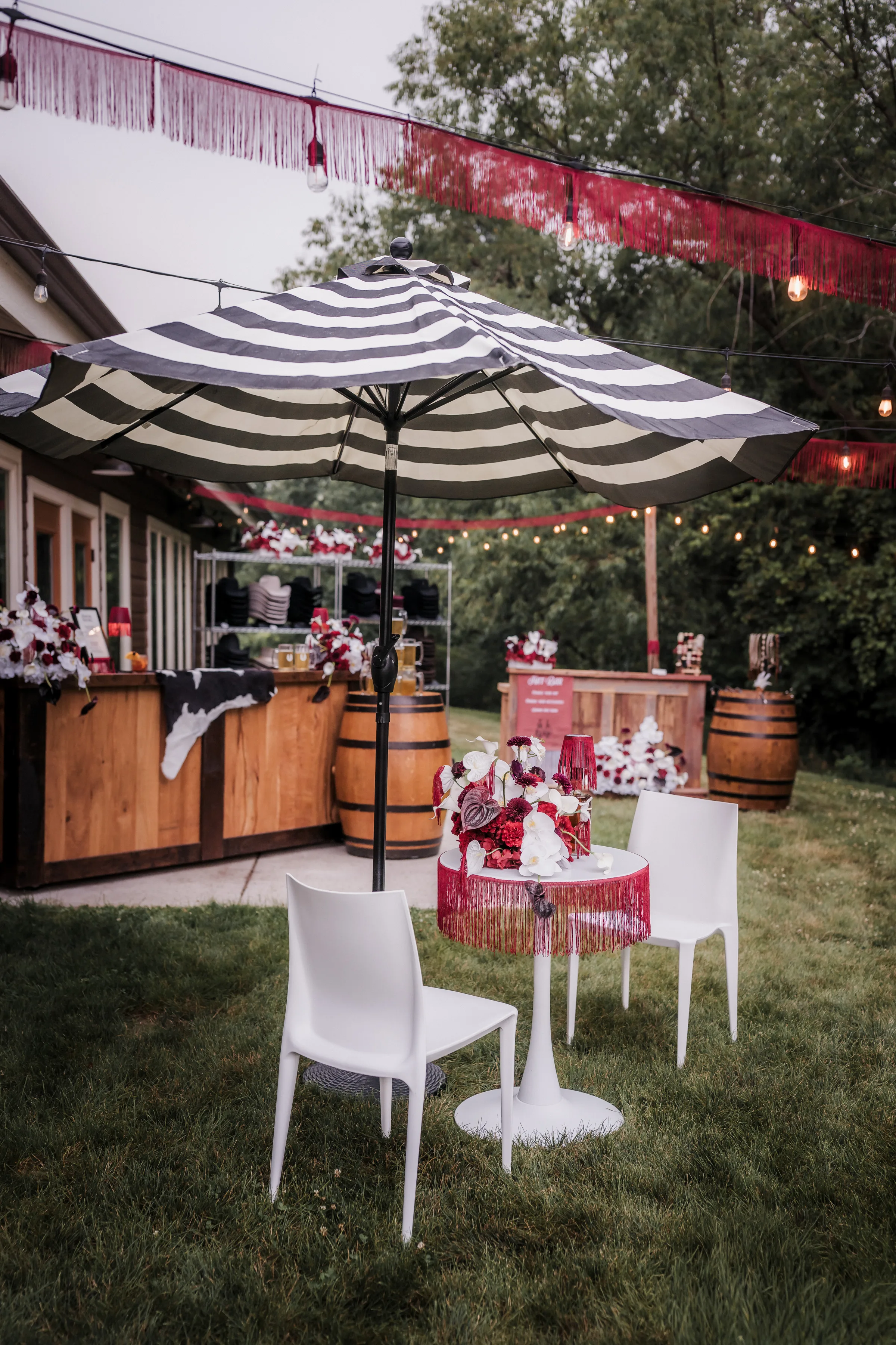 a tasseled cocktail table and two chairs sit beneath a black-and-white striped umbrella