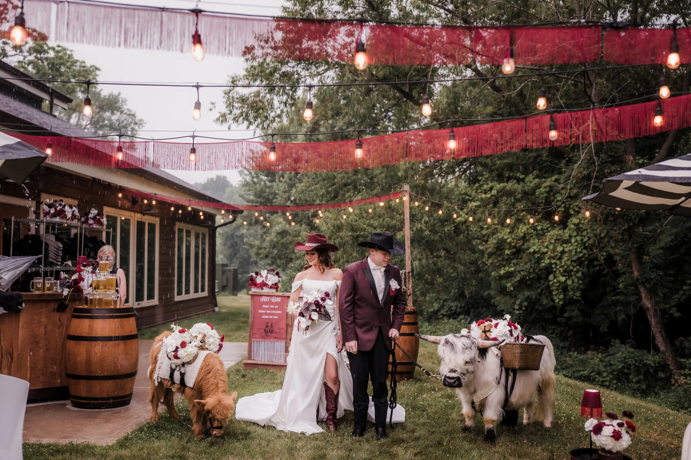 bride and groom models stand side by side at the outdoor bar and lounge at Barnwood Events in Madison, Wisconsin. Models are both wearing cowboy hats and looking down at adorable beverage steers from Tiny Acre Farms
