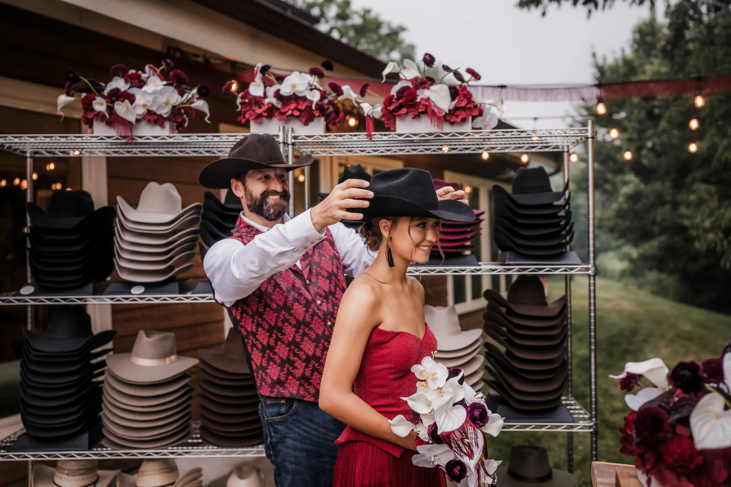 a wedding guest playfully places a black cowboy hat on the head of another wedding guest