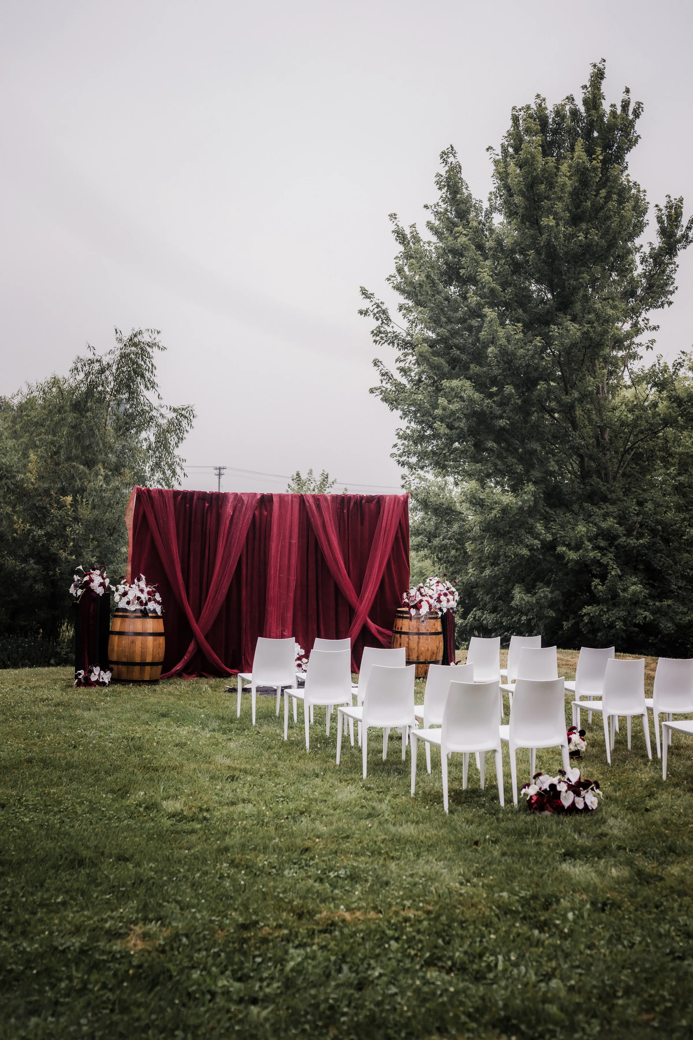 an angled view of a moody modern cowboy wedding inspiration at Barnwood Events showing white chairs, burgundy draping, and rustic wooden accents