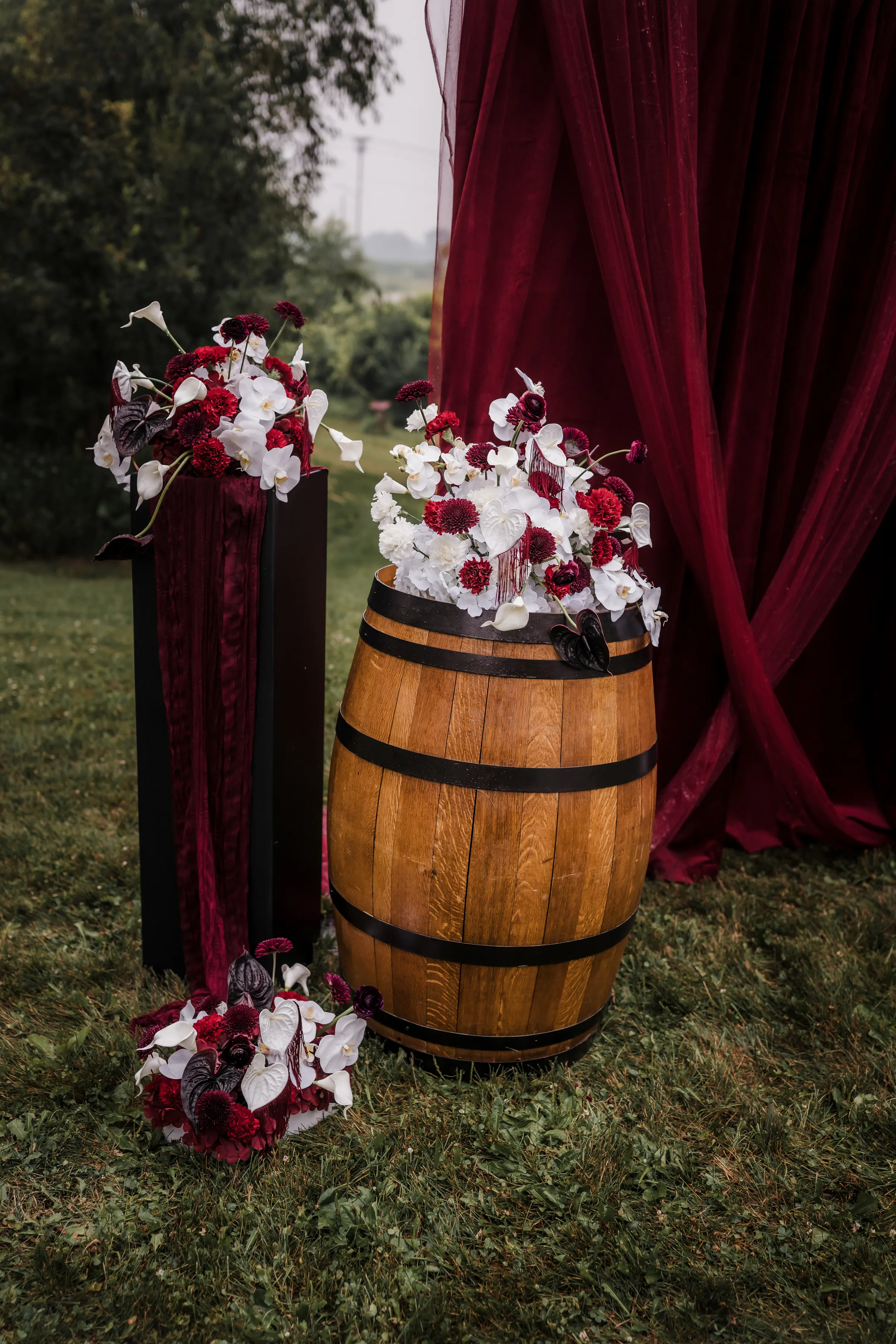a detail photo showing a rustic wooden barrel wedding décor with white, red, and burgundy florals placed on top
