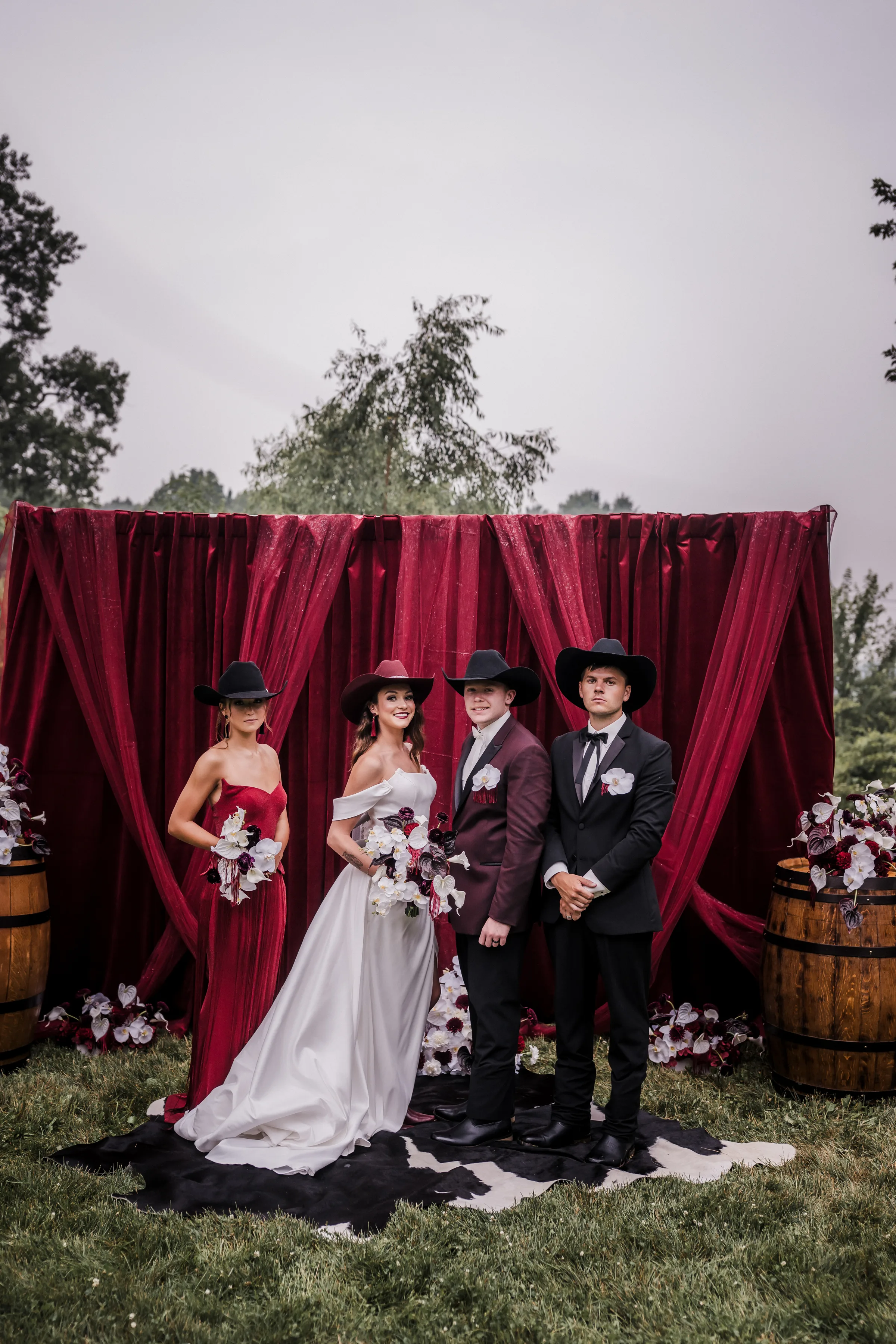 bride and groom models pose with their wedding party in front of a moody burgundy backdrop, including bridesmaid and best man