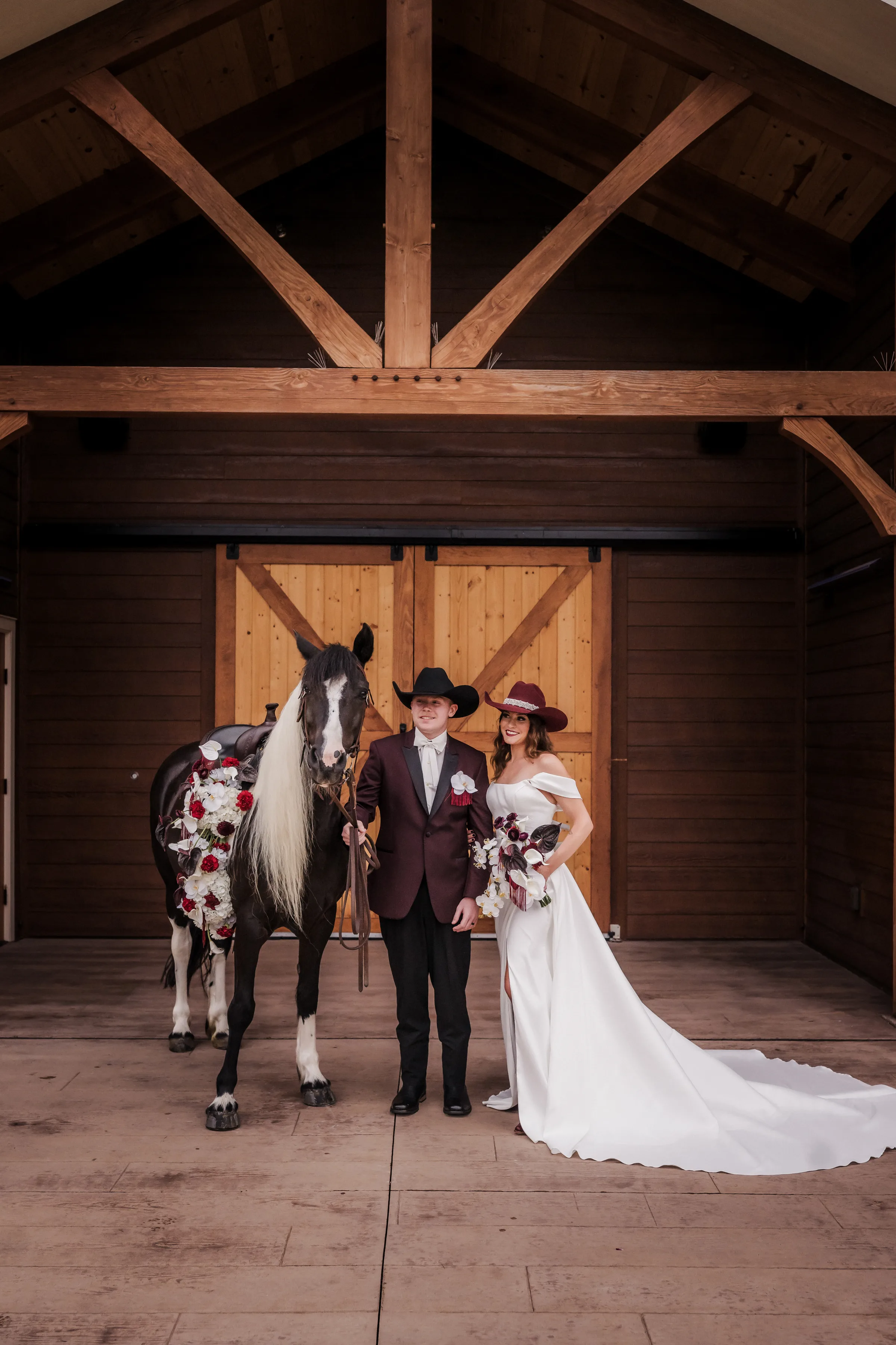 bride and groom stand beside a horse model at Barnwood Events. The horse is wearing florals from Melody Rose Designs and the couple is dressed for a moody modern cowboy wedding