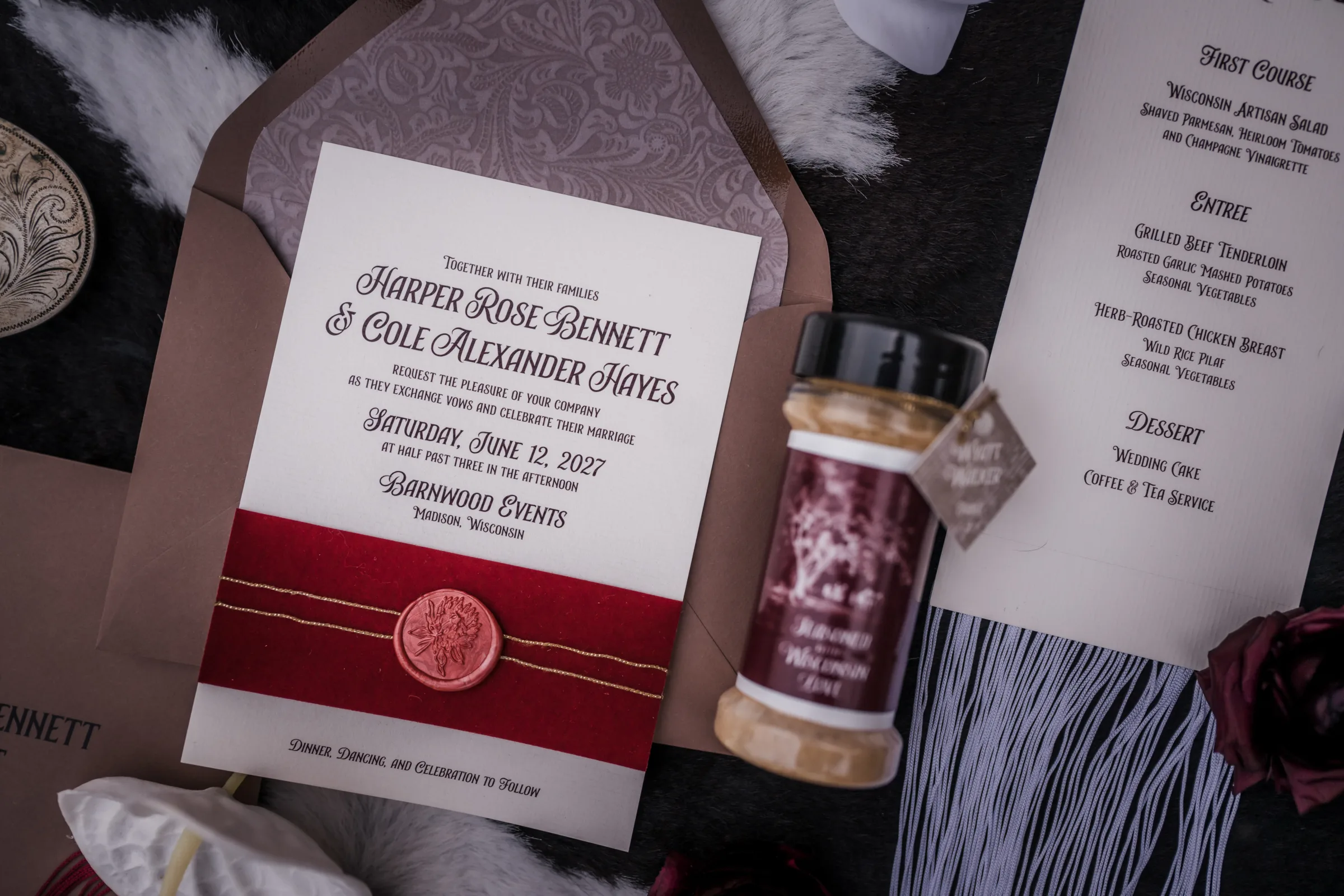 a close-up of a layered invitation by LK Bridal Studio featuring western font, burgundy and gold tie, and a shimmering wax seal