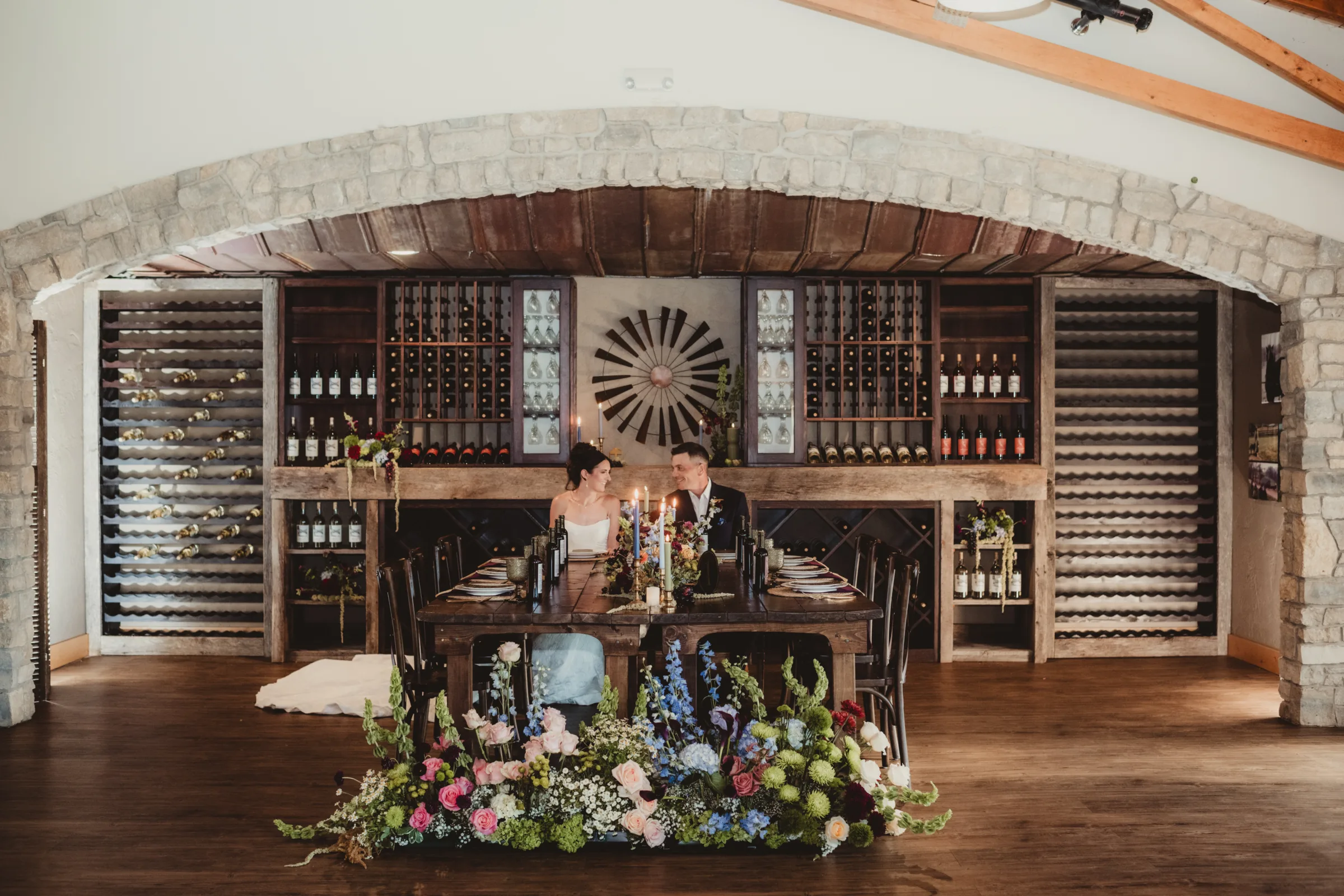 the bride and groom models sit at the head of a reception table set against Vennebu Hill's rustic wine cellar