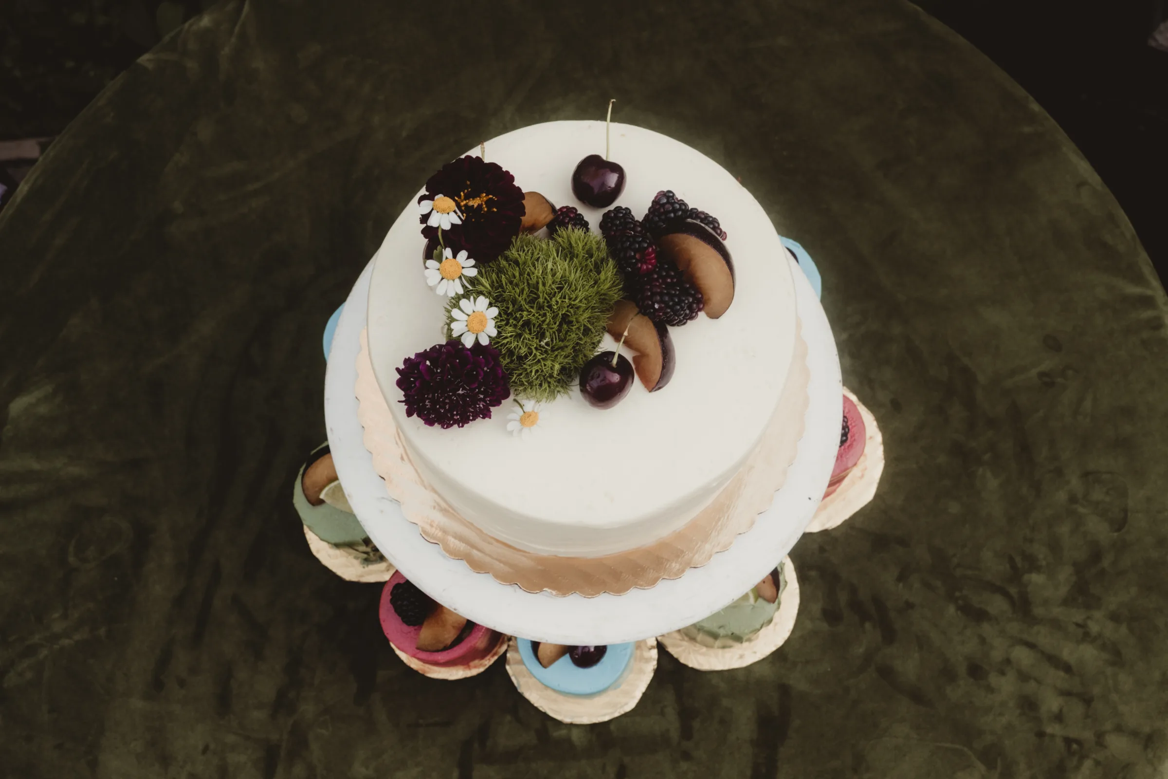 cake and dessert inspiration from Sandy Kakes showing a single tier white wedding cake on a pedestal surrounded by textured, colorful, single-serving cakes. All are topped with fruit and/or florals