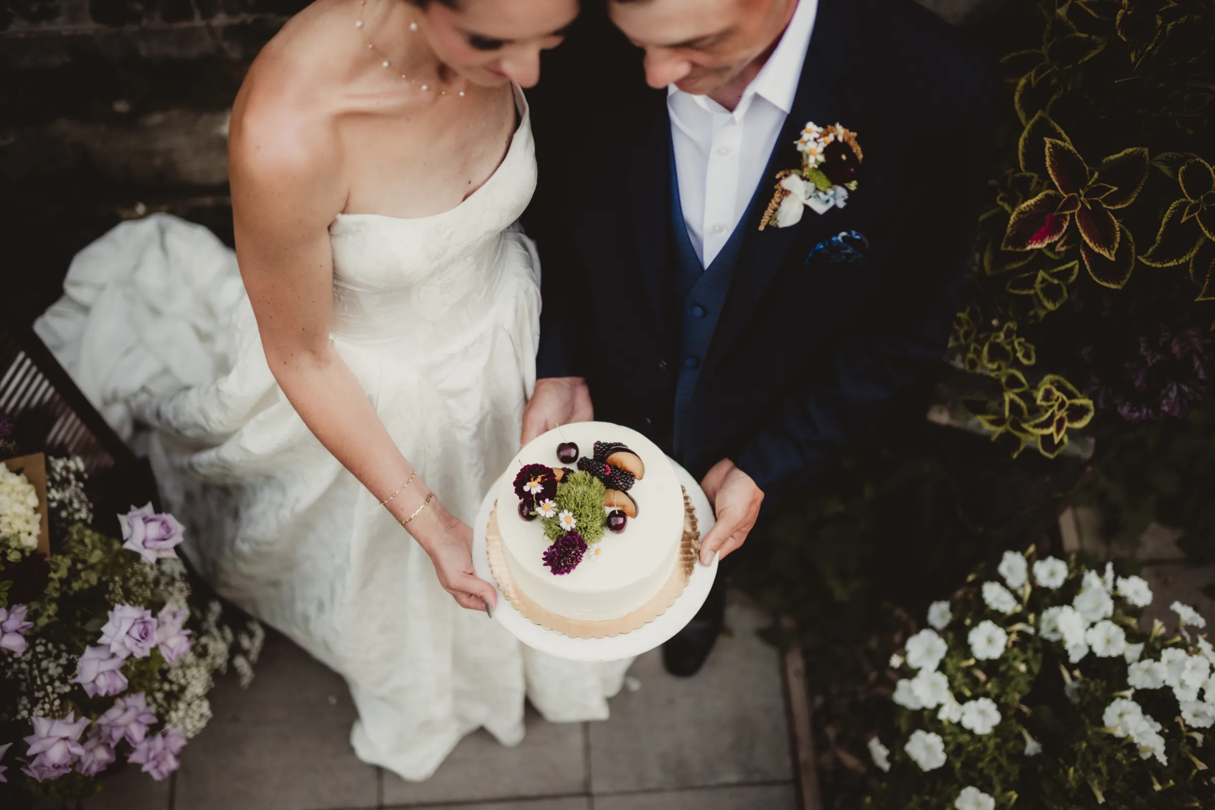 the bride and groom models present a single tier white wedding cake from Sandy Kakes topped with fruit and florals