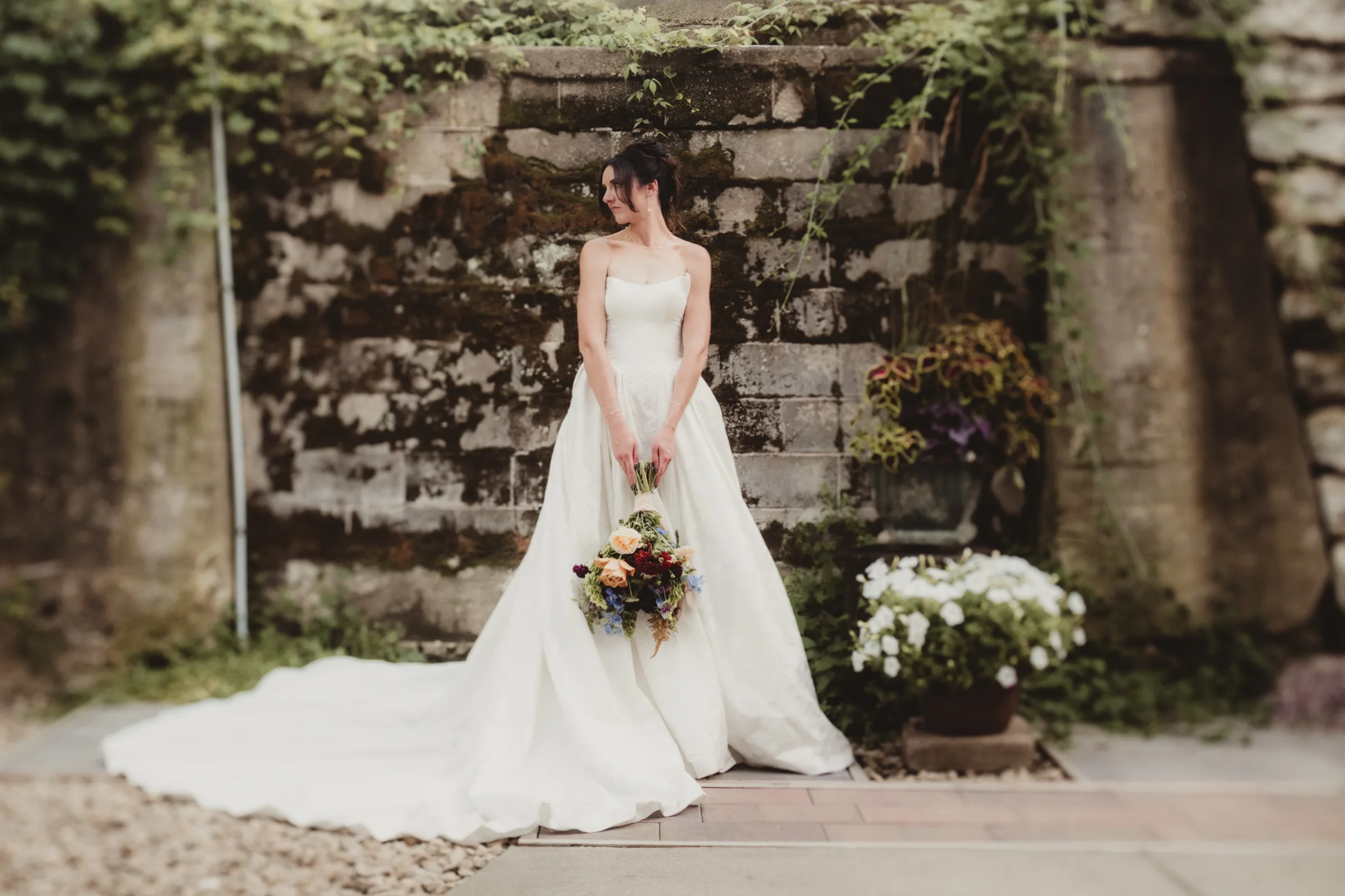 the bride stands against a brick wall holding a bouquet