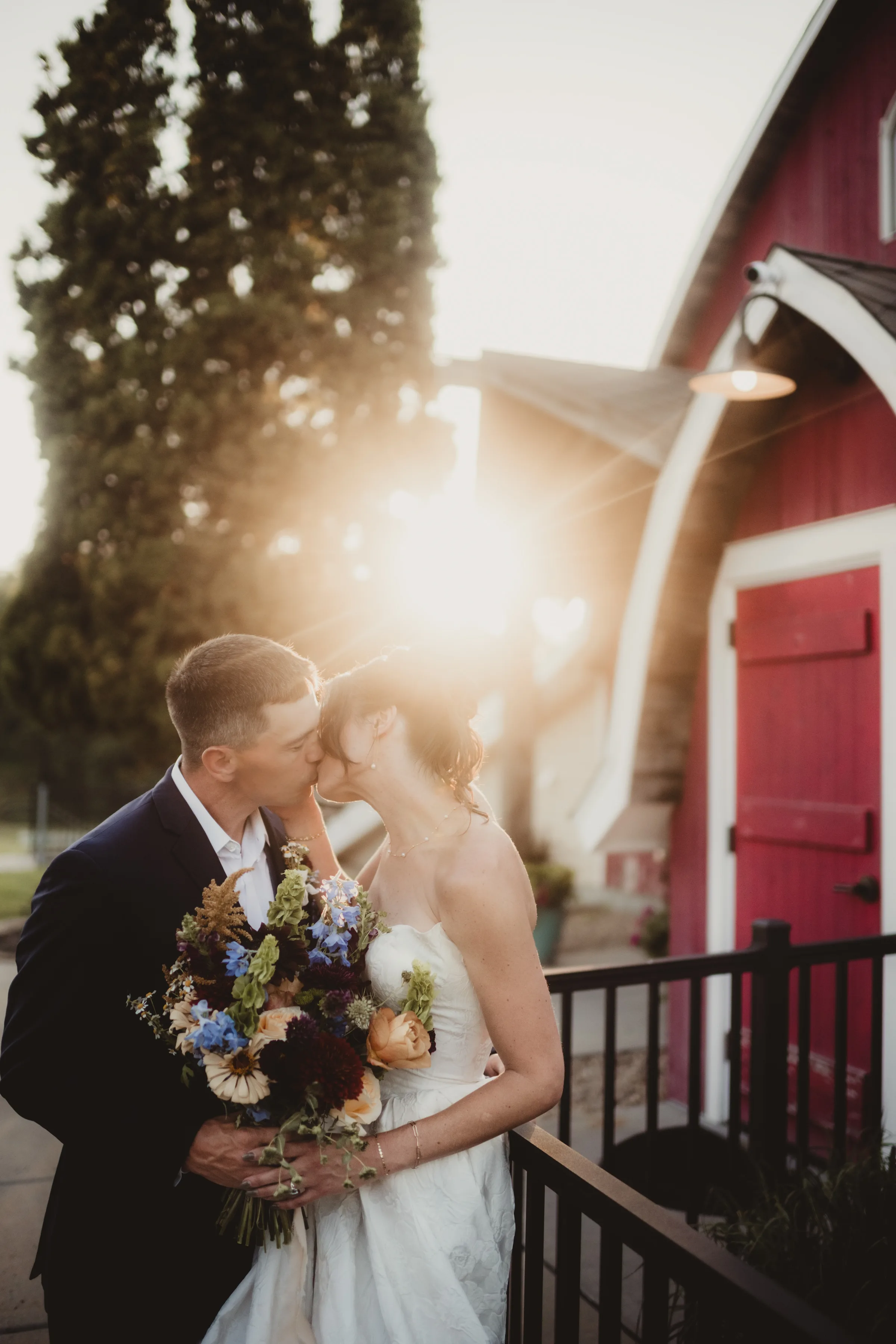 the couple shares a kiss at golden hour, with Vennebu Hill's red barn in the background