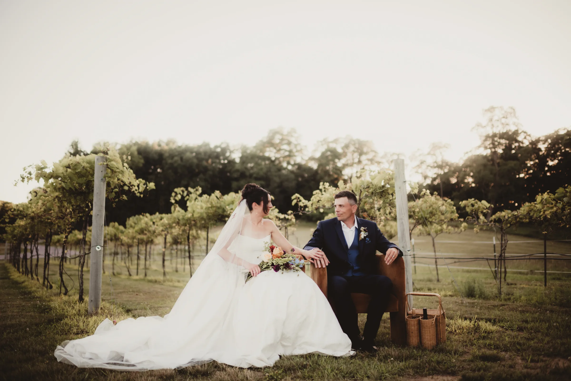 the couple holds hands, seating in Vennebu Vineyard surrounded by rows of trees