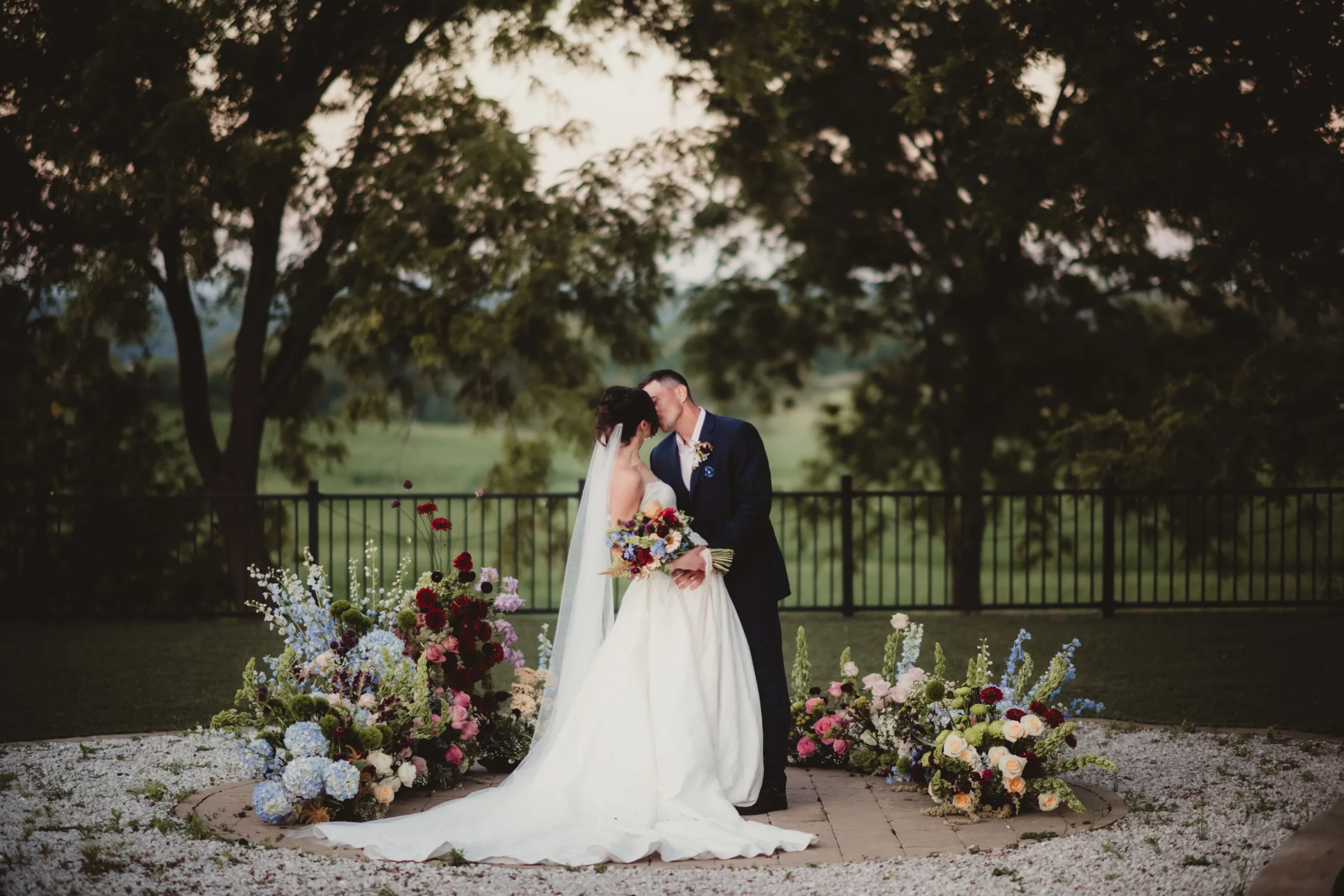 the bride and groom models share a kiss in front of a colorful, grounded floral arch wedding inspiration from Signature Events, featuring wildflower styling
