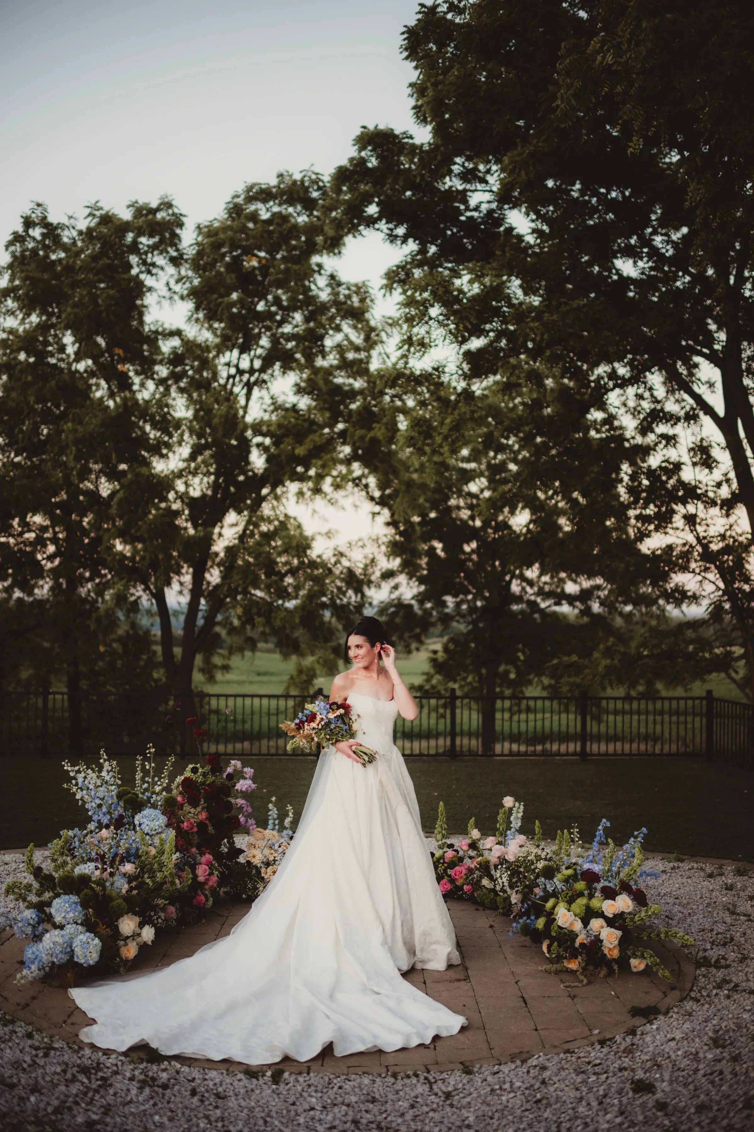 the bride model stands in front of a colorful, grounded floral arch wedding inspiration from Signature Events, featuring wildflower styling