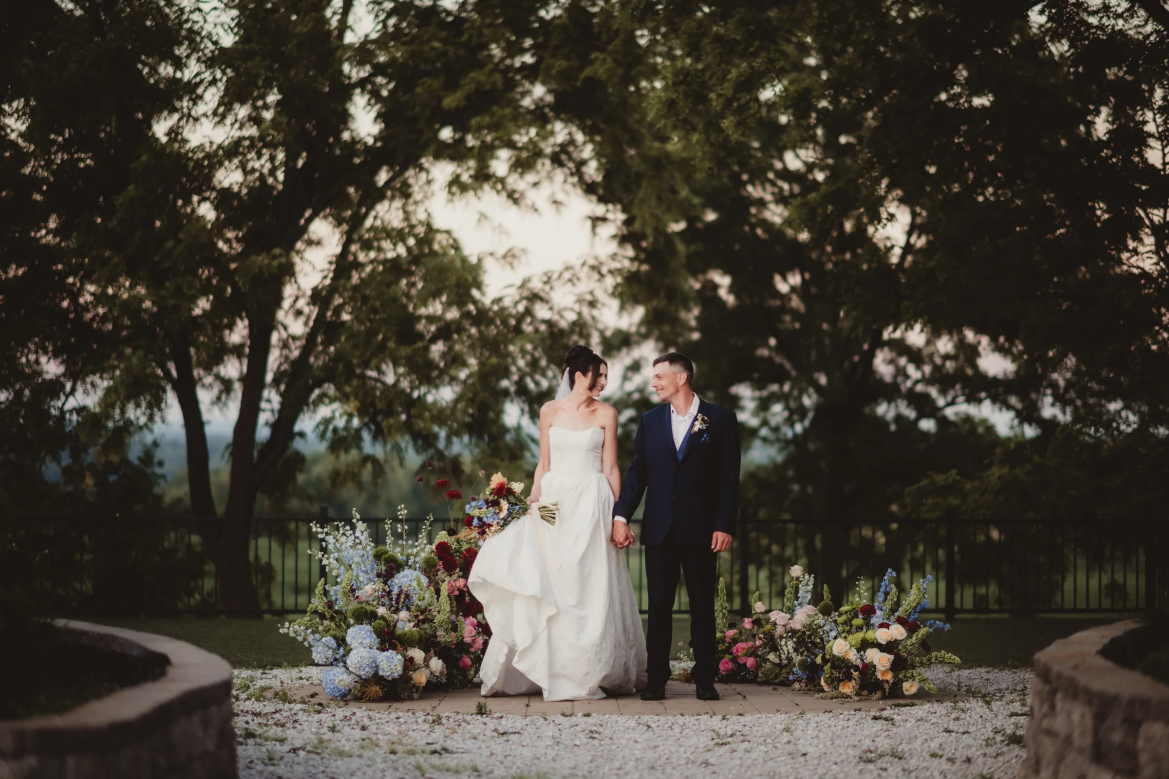 the bride and groom models hold hands in front of a colorful, grounded floral arch wedding inspiration from Signature Events, featuring wildflower styling