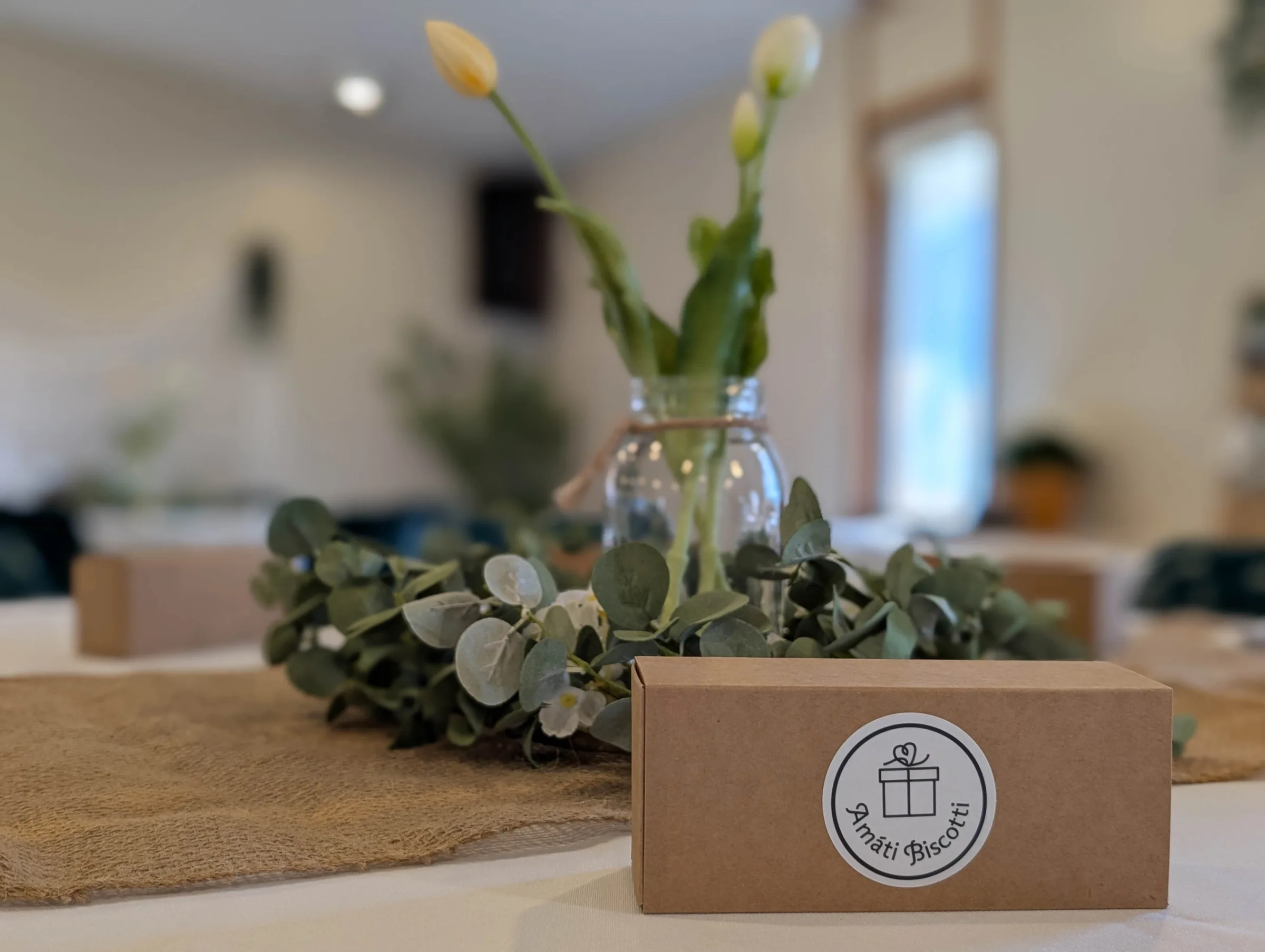 Amati Biscotti kraft favor box on a wedding reception table with eucalyptus greenery and bud vase