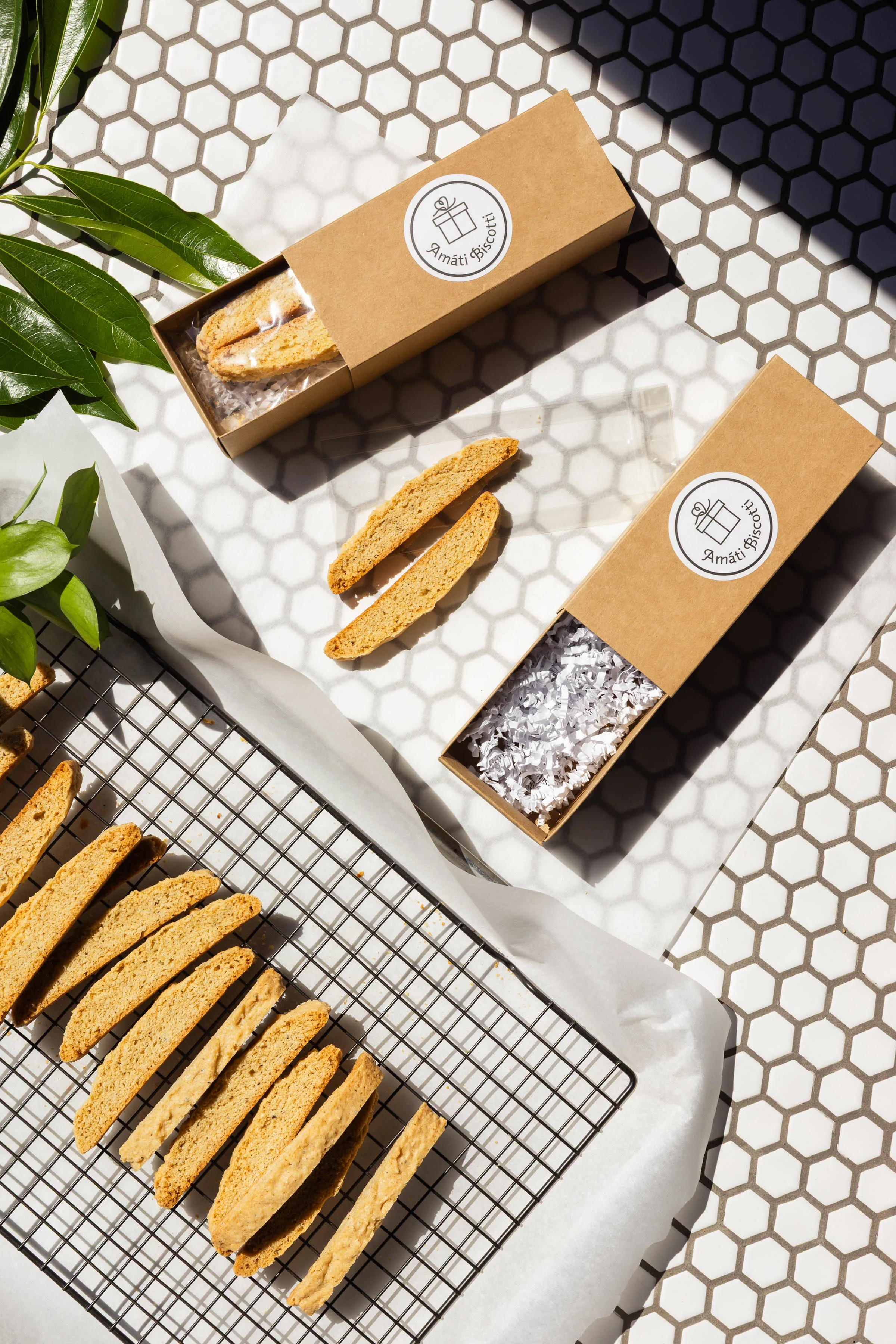 Amati Biscotti gift boxes being packaged with sliced biscotti cooling on a rack nearby