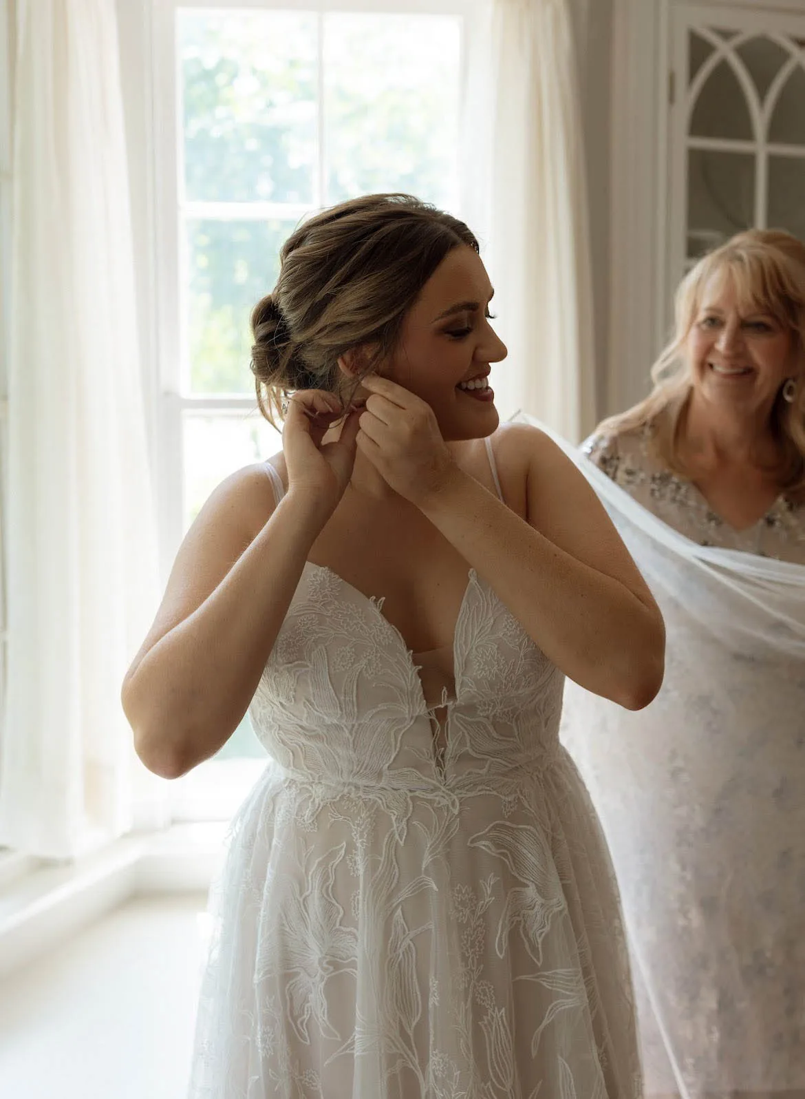 MAIE House bridal hair styled in a loose braided updo — bride putting in earrings while getting ready, mother helping with the veil