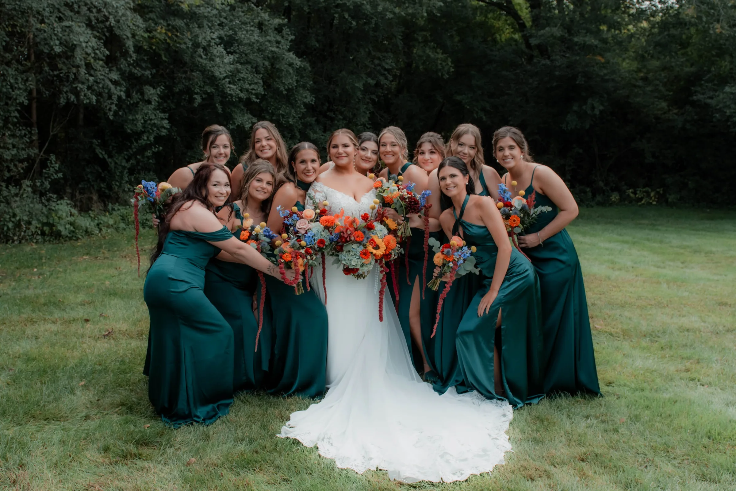 MAIE House hair and makeup for bride and large bridesmaid party — group portrait in emerald dresses with colorful wildflower bouquets
