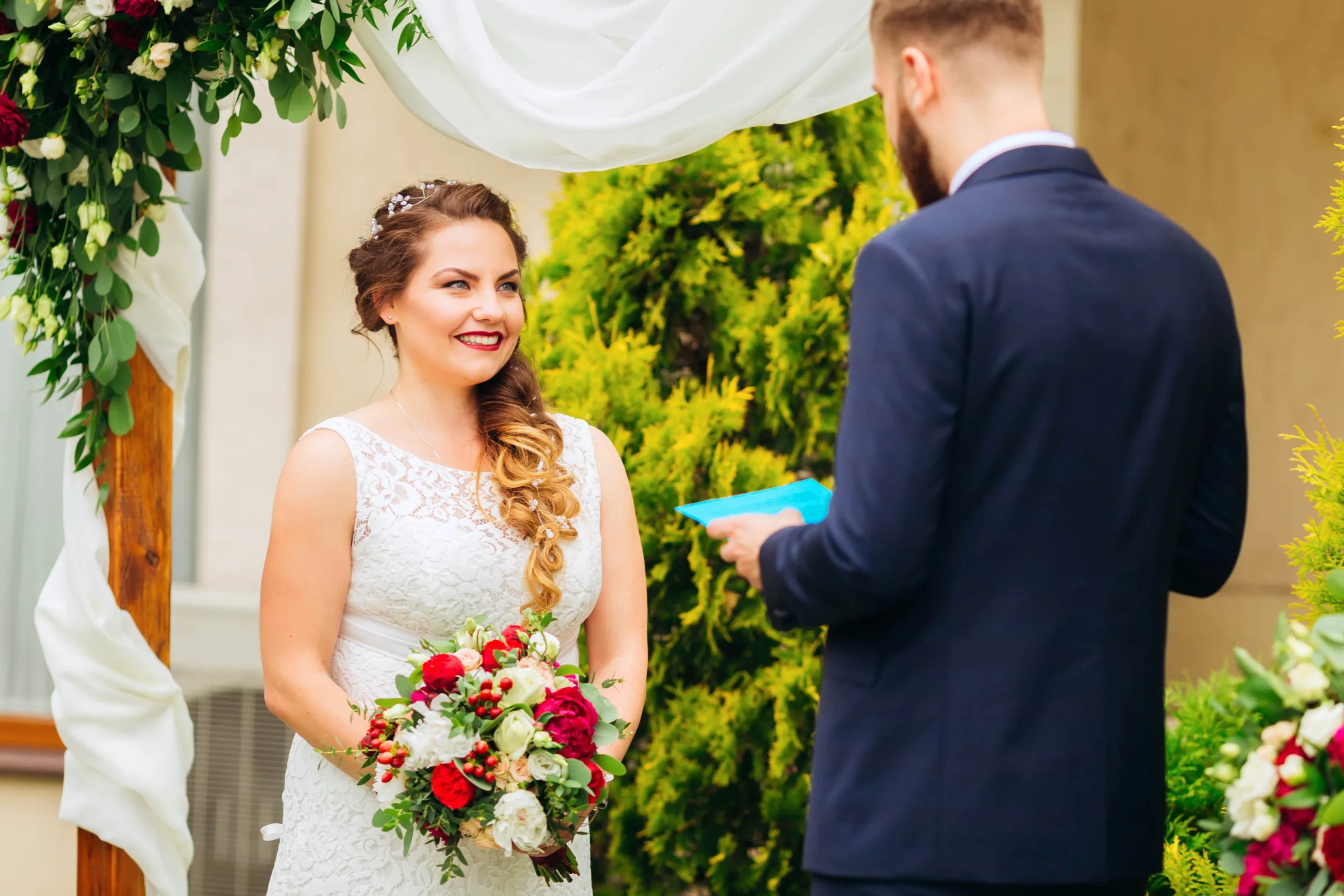 A beautiful bride stands near the decorated arch and holds a wed