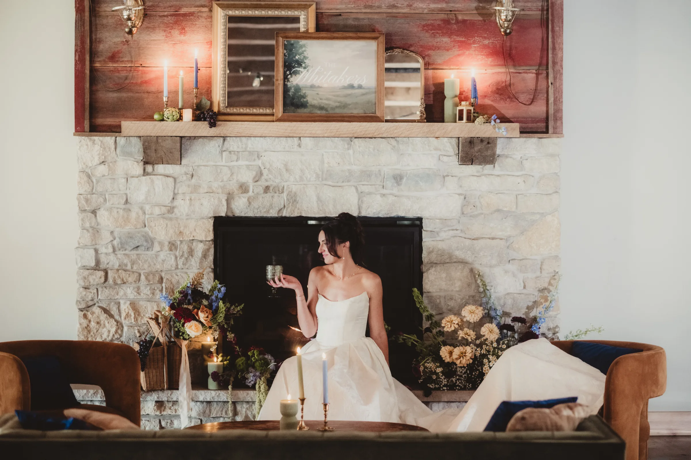 the bride sits by a cozy fireplace setting surrounded by florals and glowing candles at Vennebu Hill in Baraboo, Wisconsin