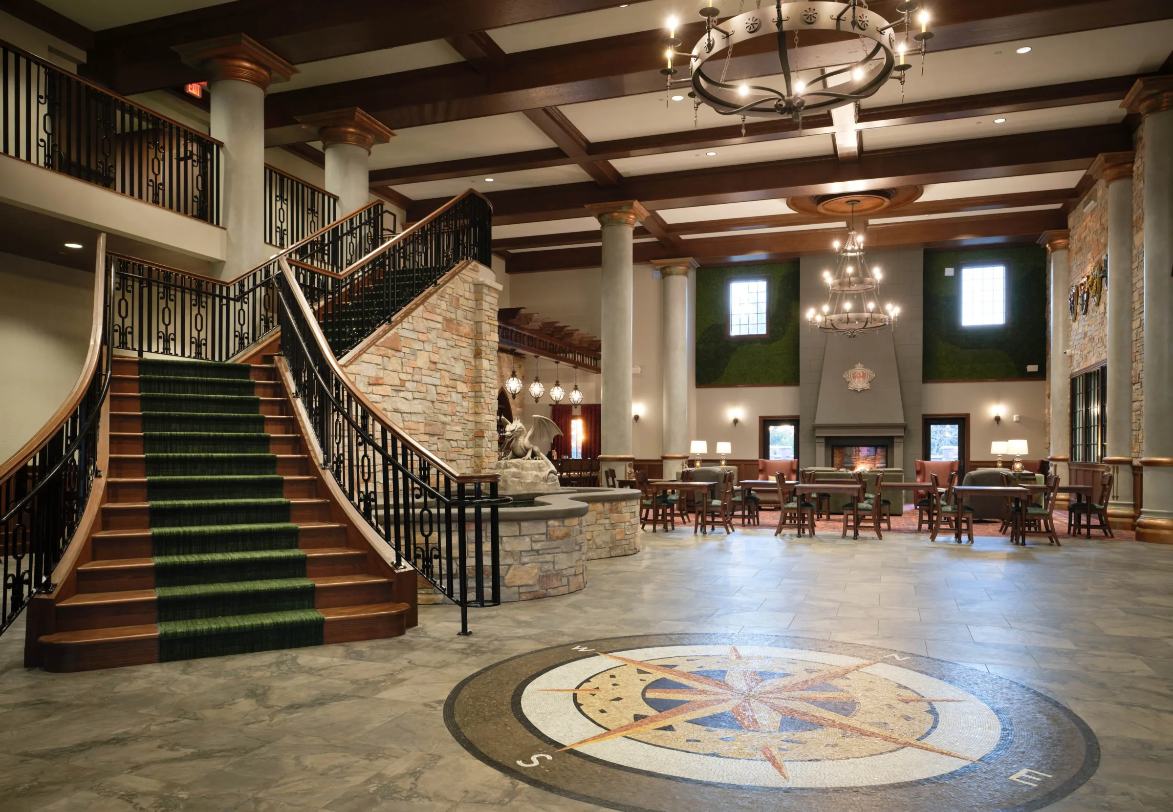 Grand lobby entrance at Dellshire Resort, a luxury hotel and wedding venue in Wisconsin Dells, featuring a dramatic stone staircase, central compass floor mosaic, and rustic fireplace lounge.