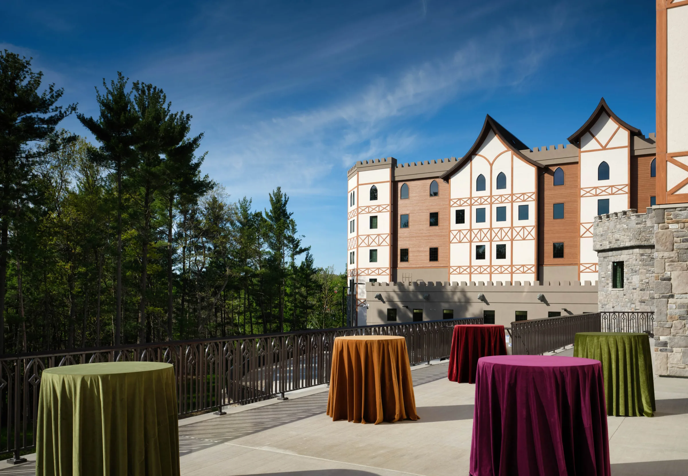 Outdoor wedding cocktail hour terrace at Dellshire Resort, a premier Wisconsin Dells wedding venue, featuring high-top tables with colorful velvet linens and a forest backdrop.