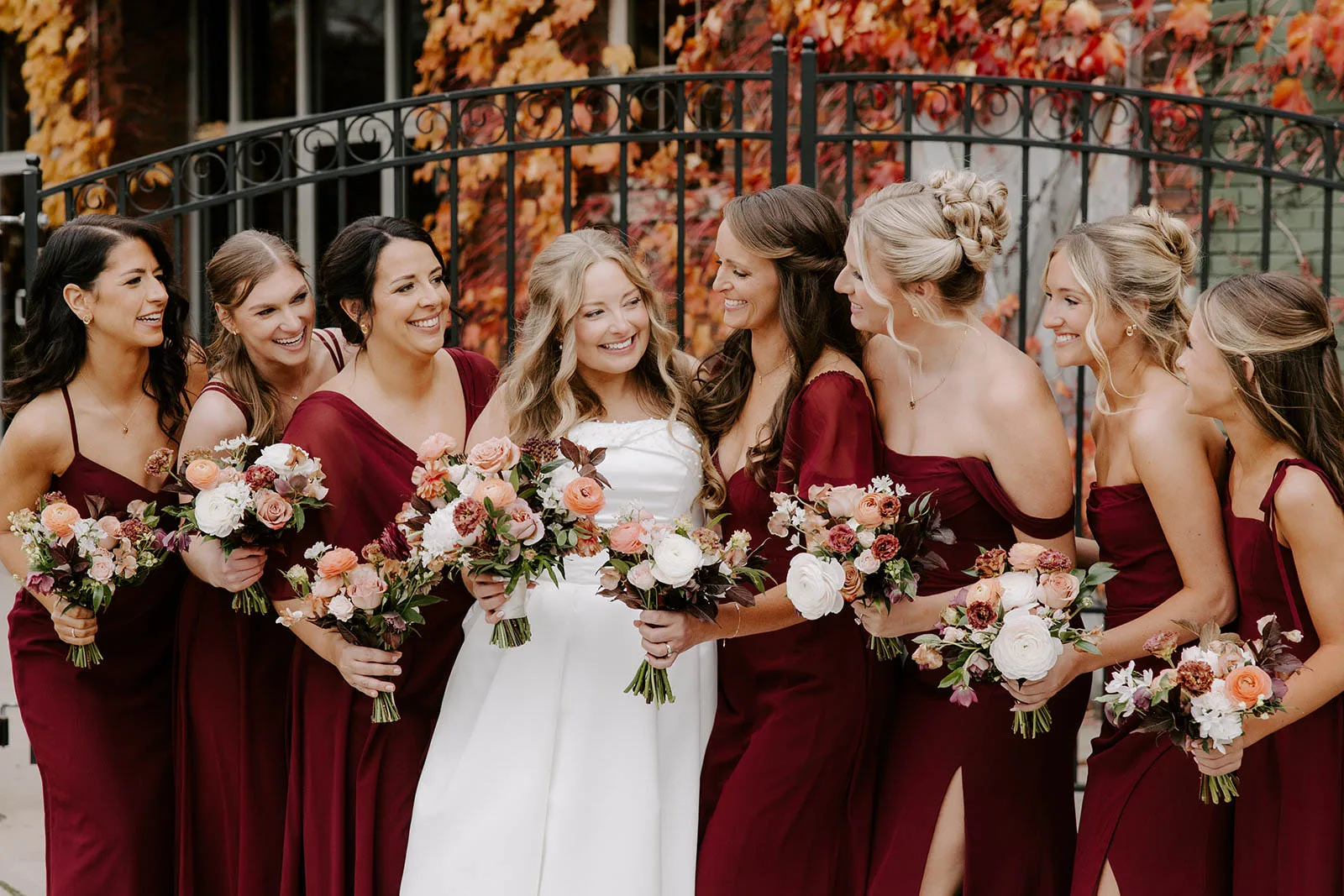 Bride and bridesmaids in burgundy dresses showing off various half-up and updo wedding hairstyles by JJ Bridal Artistry.