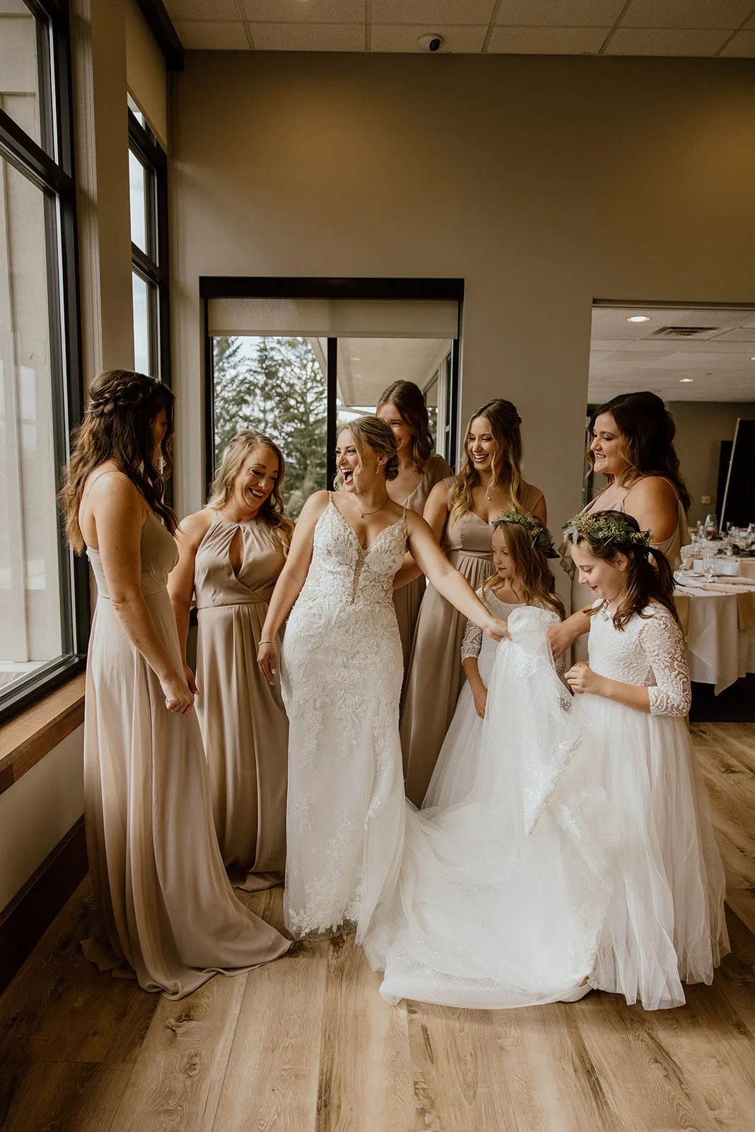 Laughing bride and her bridesmaids in neutral gowns showing off wedding hairstyles and natural makeup by JJ Bridal Artistry.