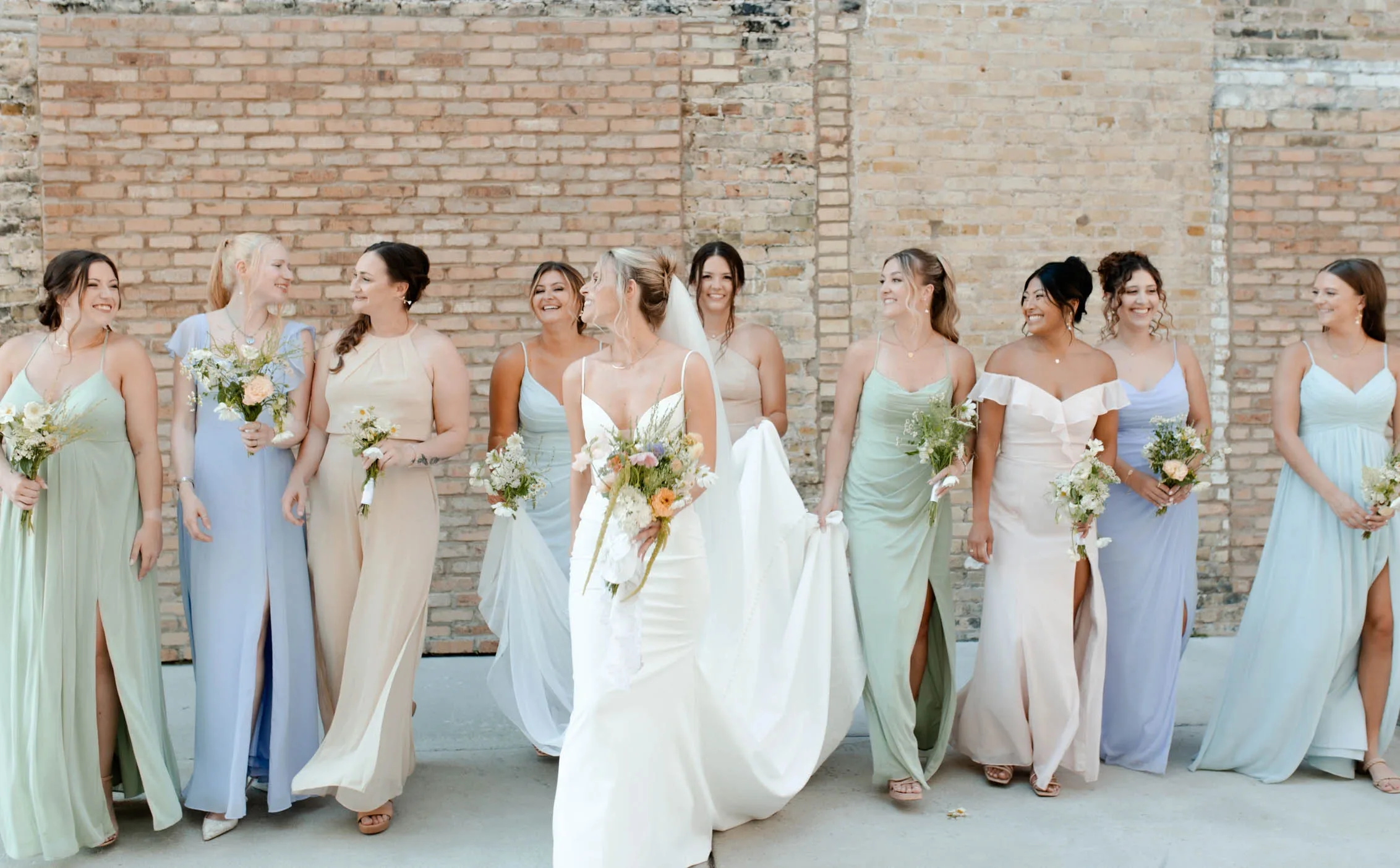 Bride and her bridesmaids in pastel mix-and-match dresses showing off individual wedding hairstyles and makeup by JJ Bridal Artistry.
