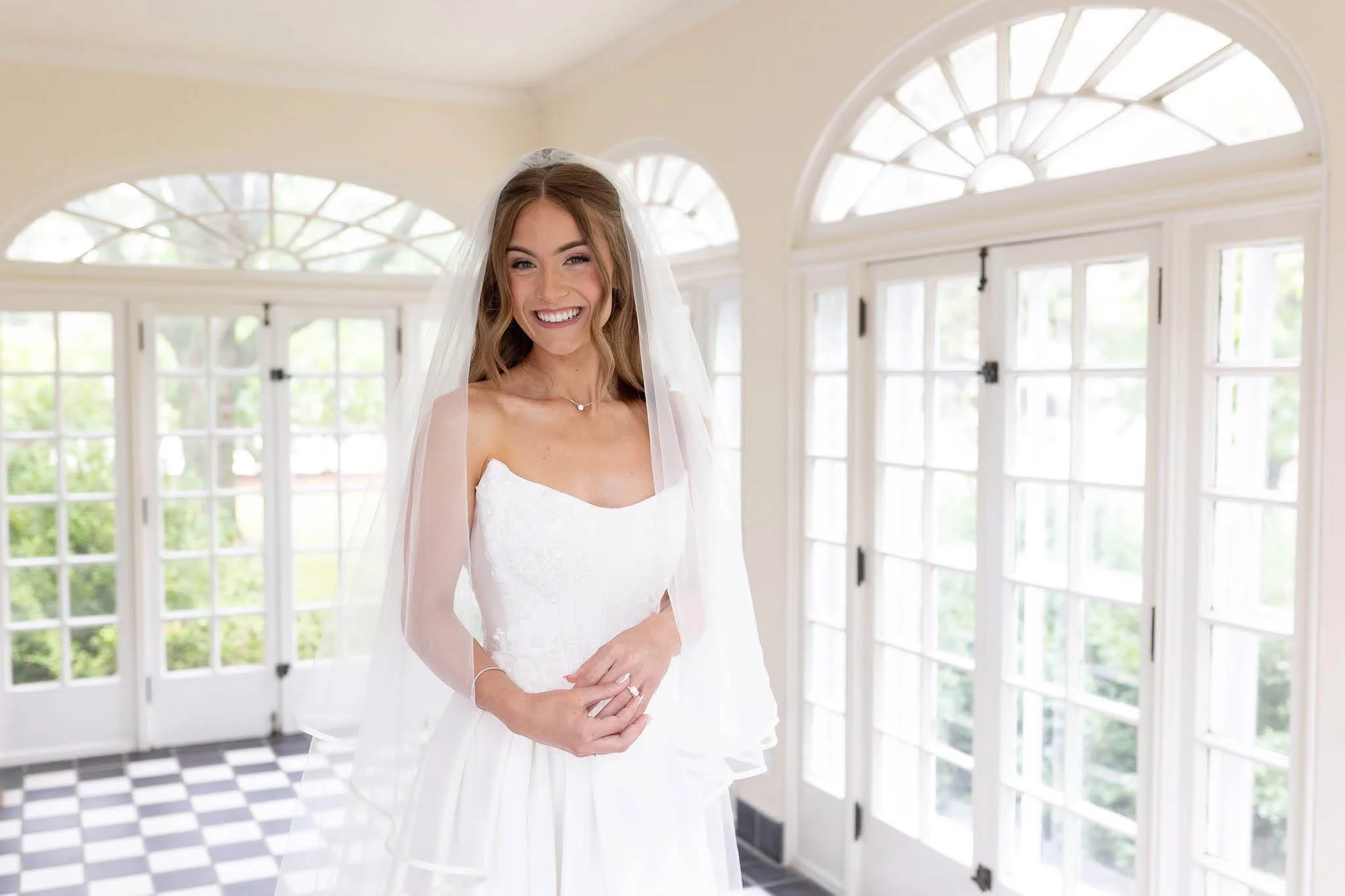 Smiling bride with soft romantic bridal makeup and long wavy half-up hair styled by JJ Bridal Artistry.
